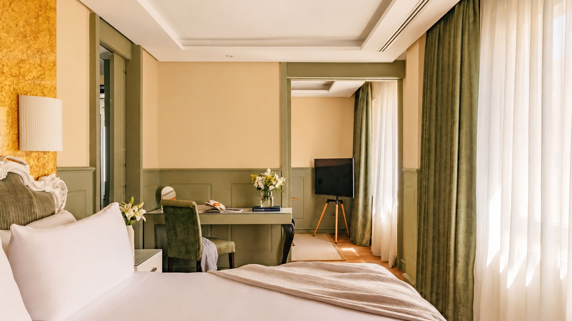 Elegant hotel room with large bed, writing desk, TV, and green trim.