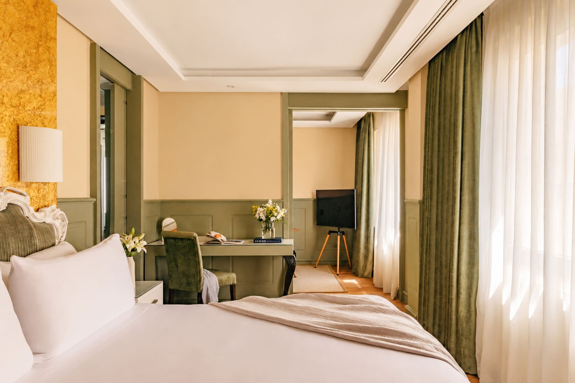 Elegant hotel room with large bed, writing desk, TV, and green trim.