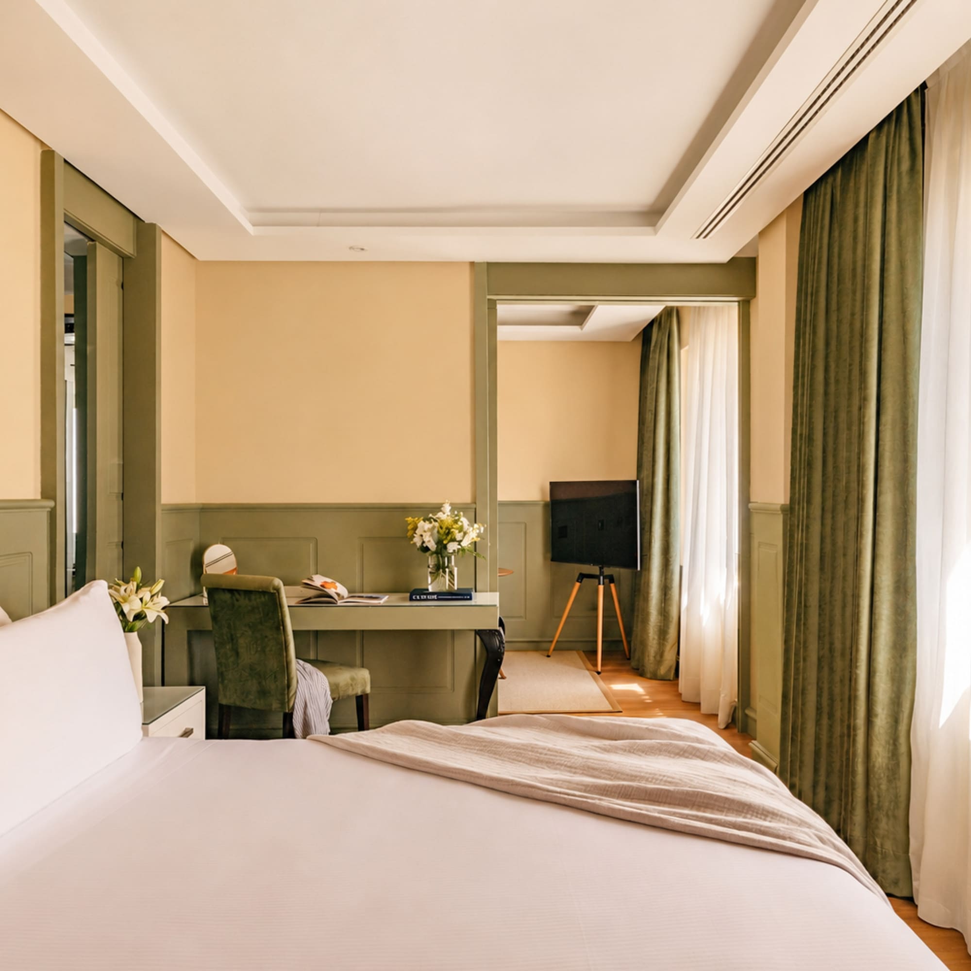 Elegant hotel room with large bed, writing desk, TV, and green trim.