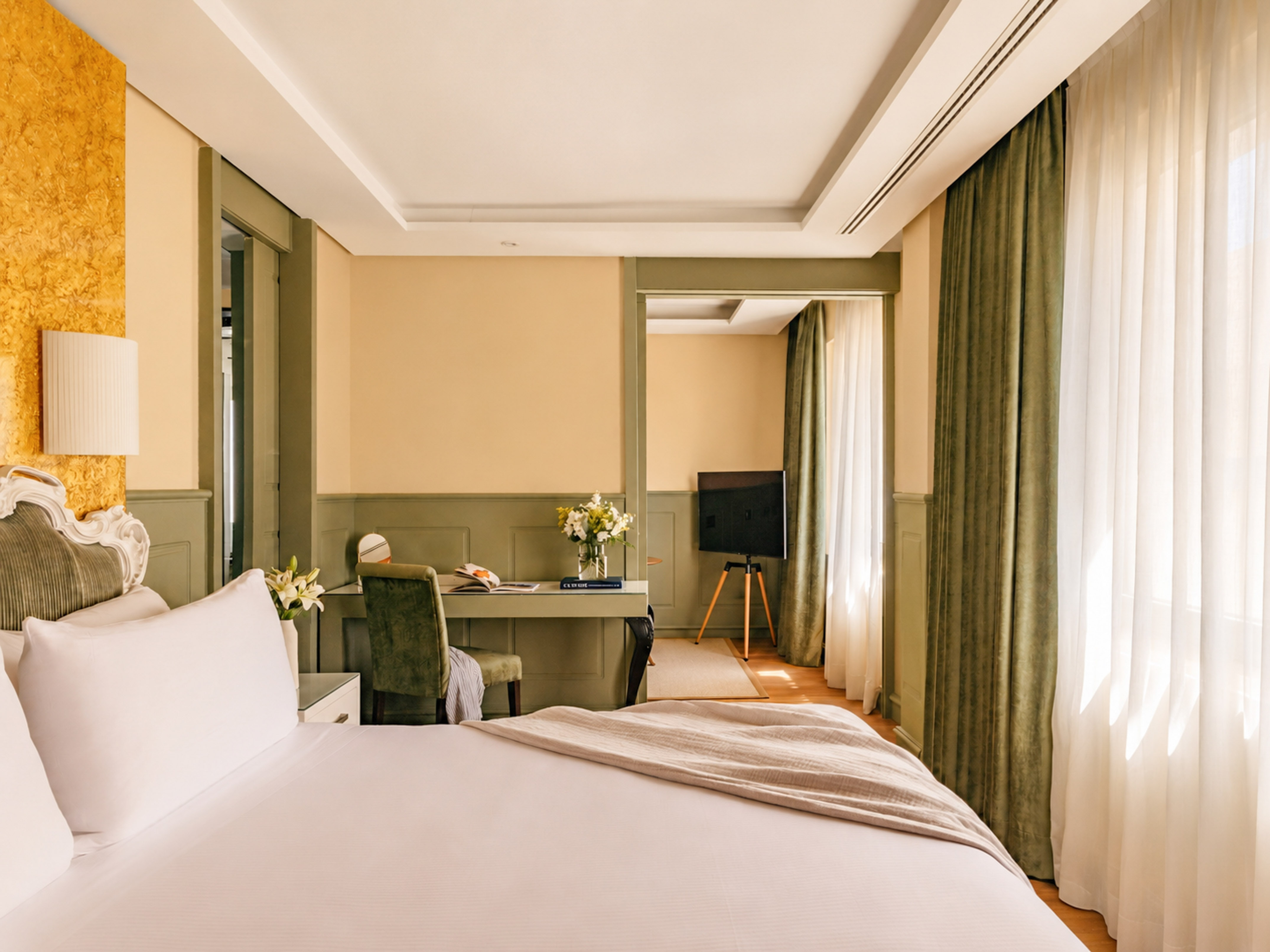 Elegant hotel room with large bed, writing desk, TV, and green trim.