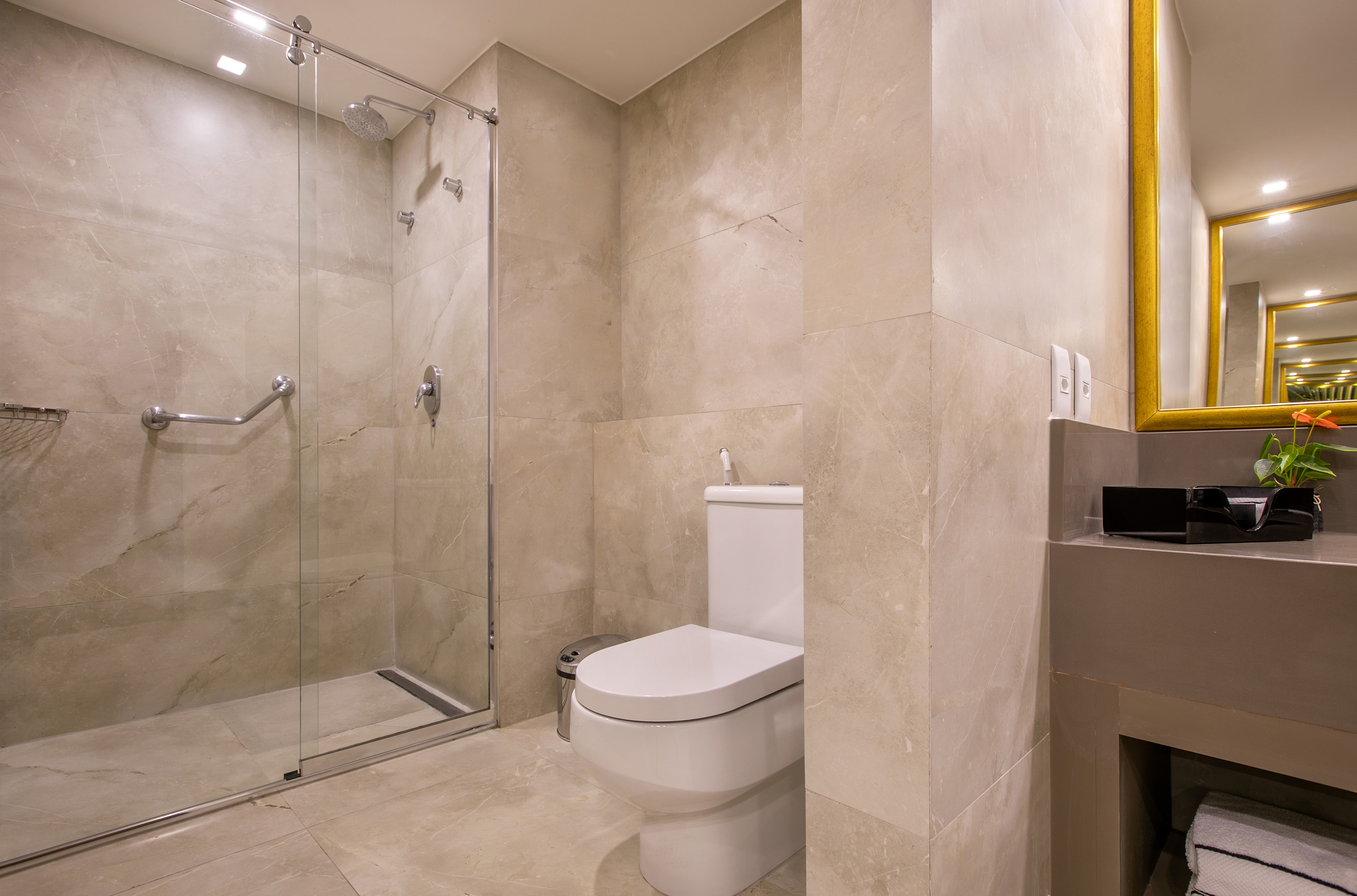 Modern tiled bathroom with glass shower, white toilet, and gold mirror.