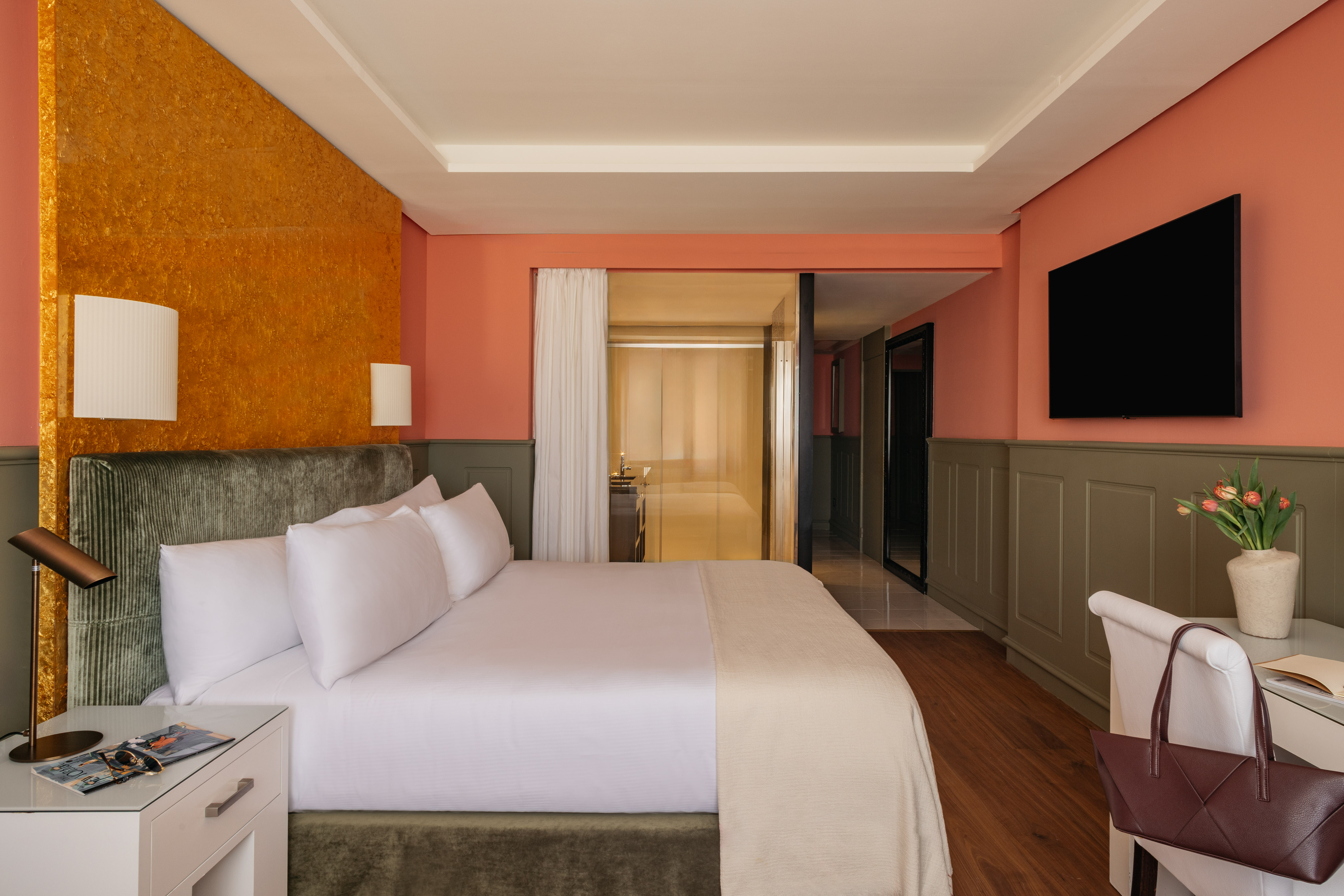 Modern hotel bedroom with vibrant orange textured wall, large bed, and TV.