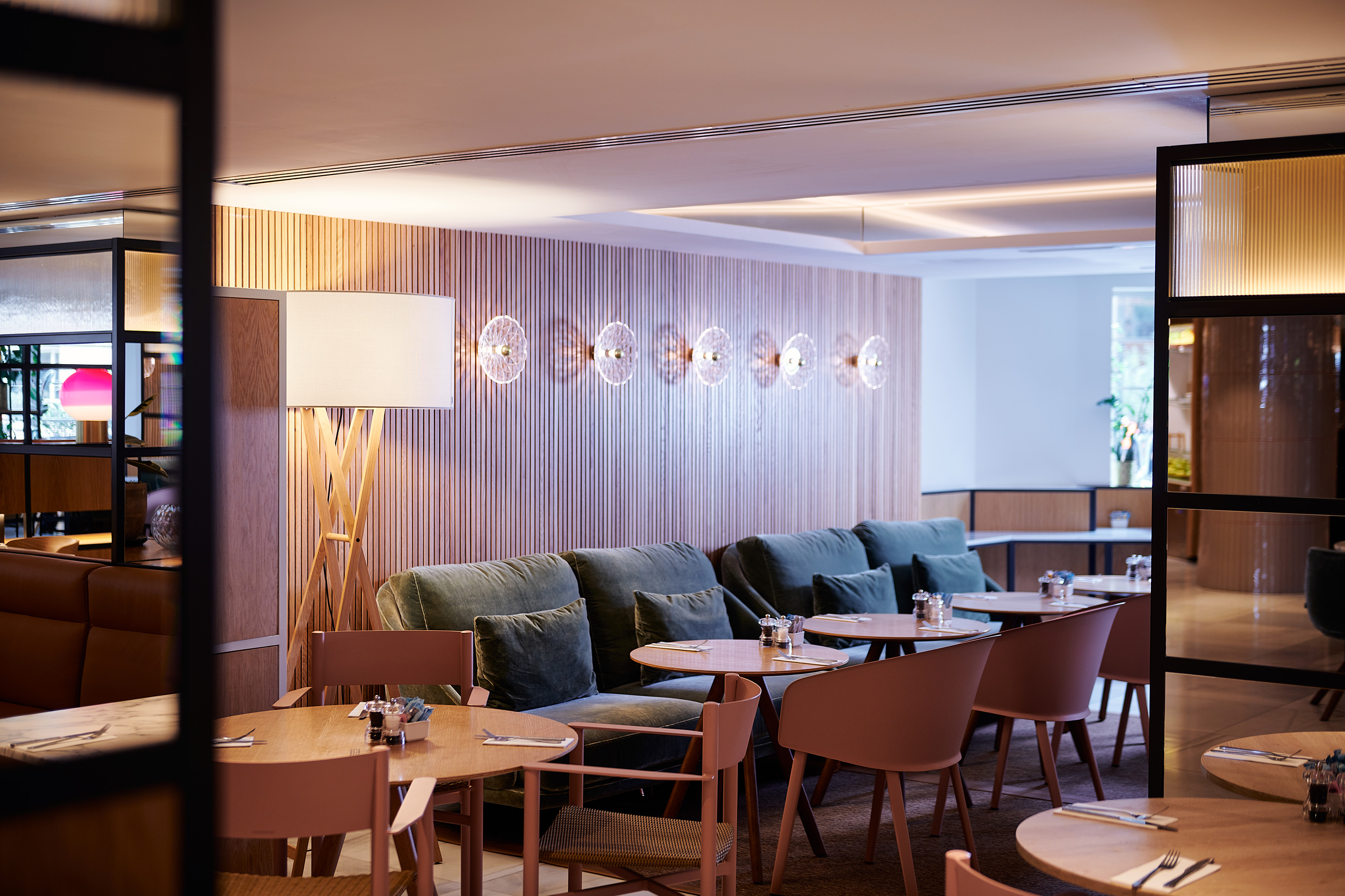 Modern restaurant dining area with green booths, wooden tables, and warm lighting.