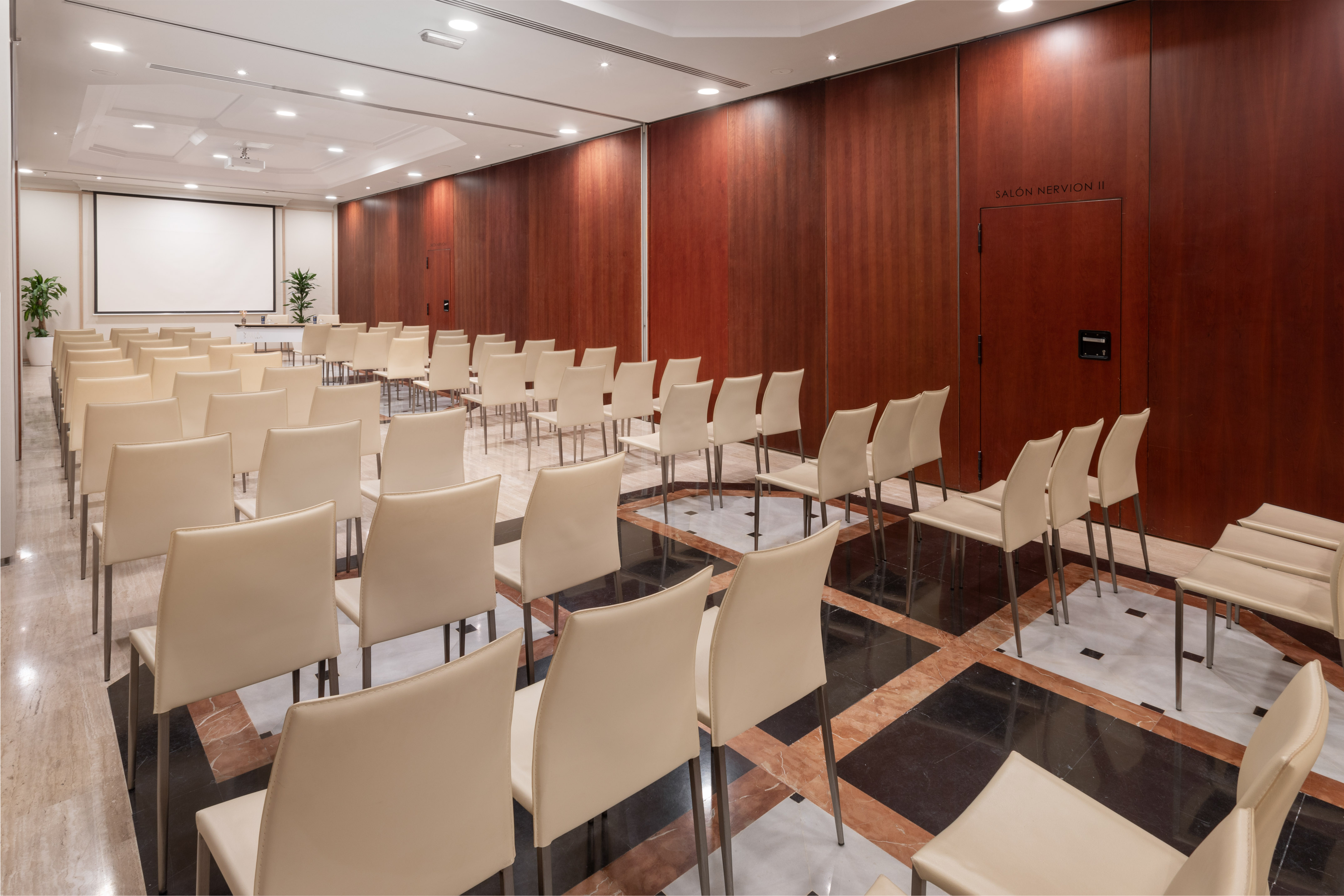 Conference room with rows of chairs, projector screen, and wood paneling.