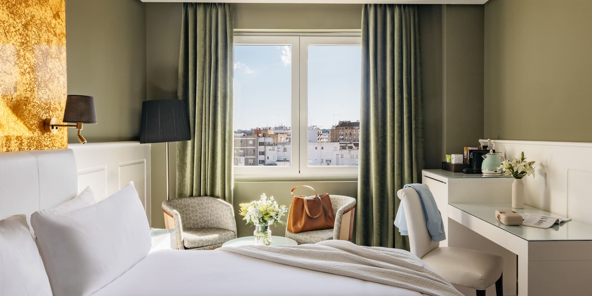 Habitación de hotel con cama, ventana a la ciudad, escritorio y sillones.