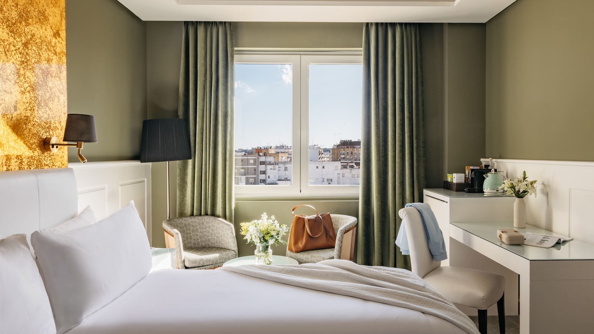 Habitación de hotel con cama, ventana a la ciudad, escritorio y sillones.
