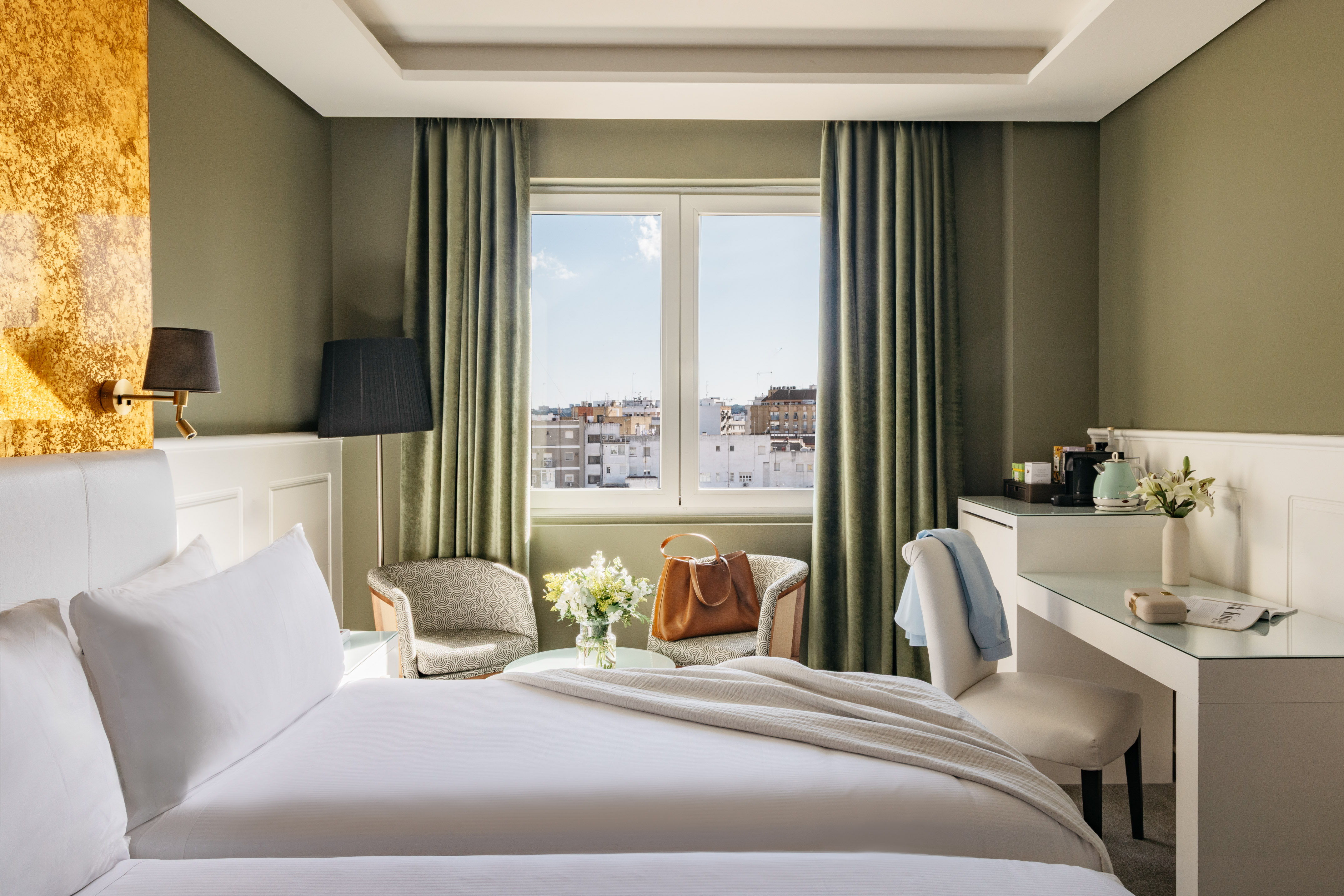Habitación de hotel con cama, ventana a la ciudad, escritorio y sillones.