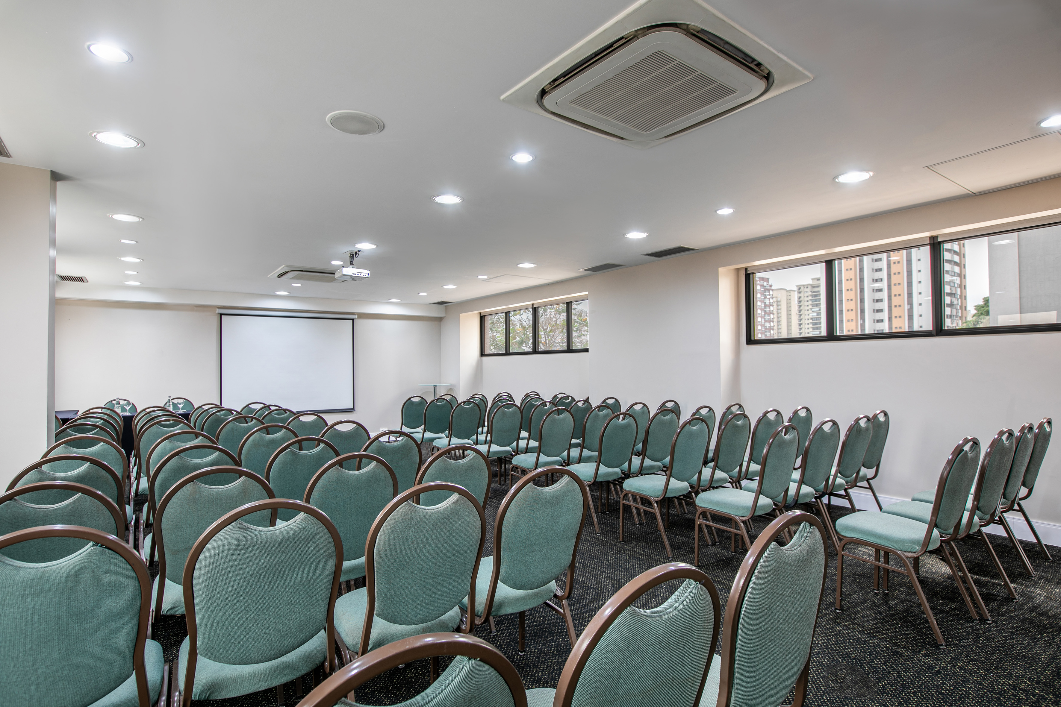 Modern meeting room with teal chairs, projector screen, and city view.
