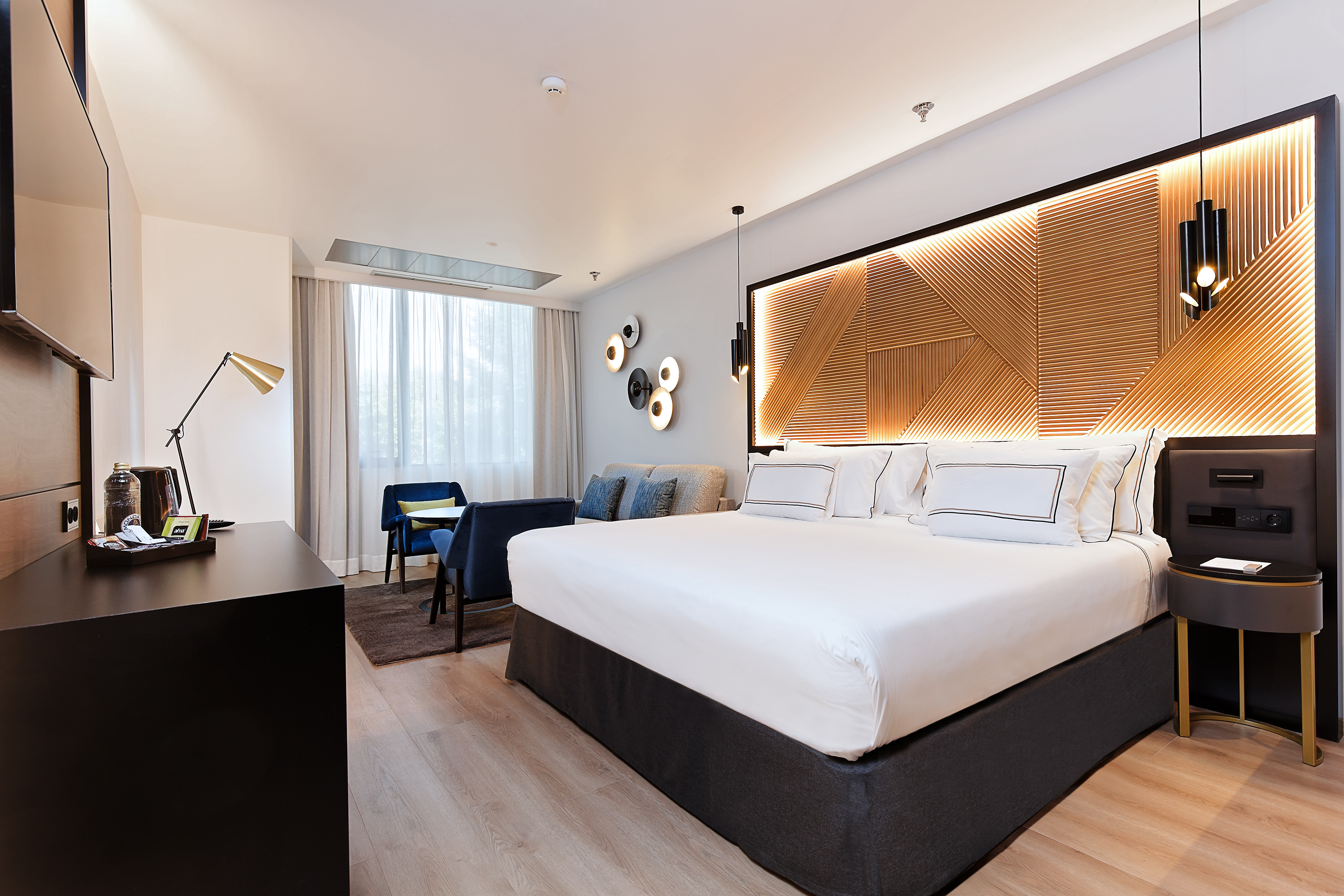 Luxury hotel room with king bed, illuminated wood headboard, and modern seating.