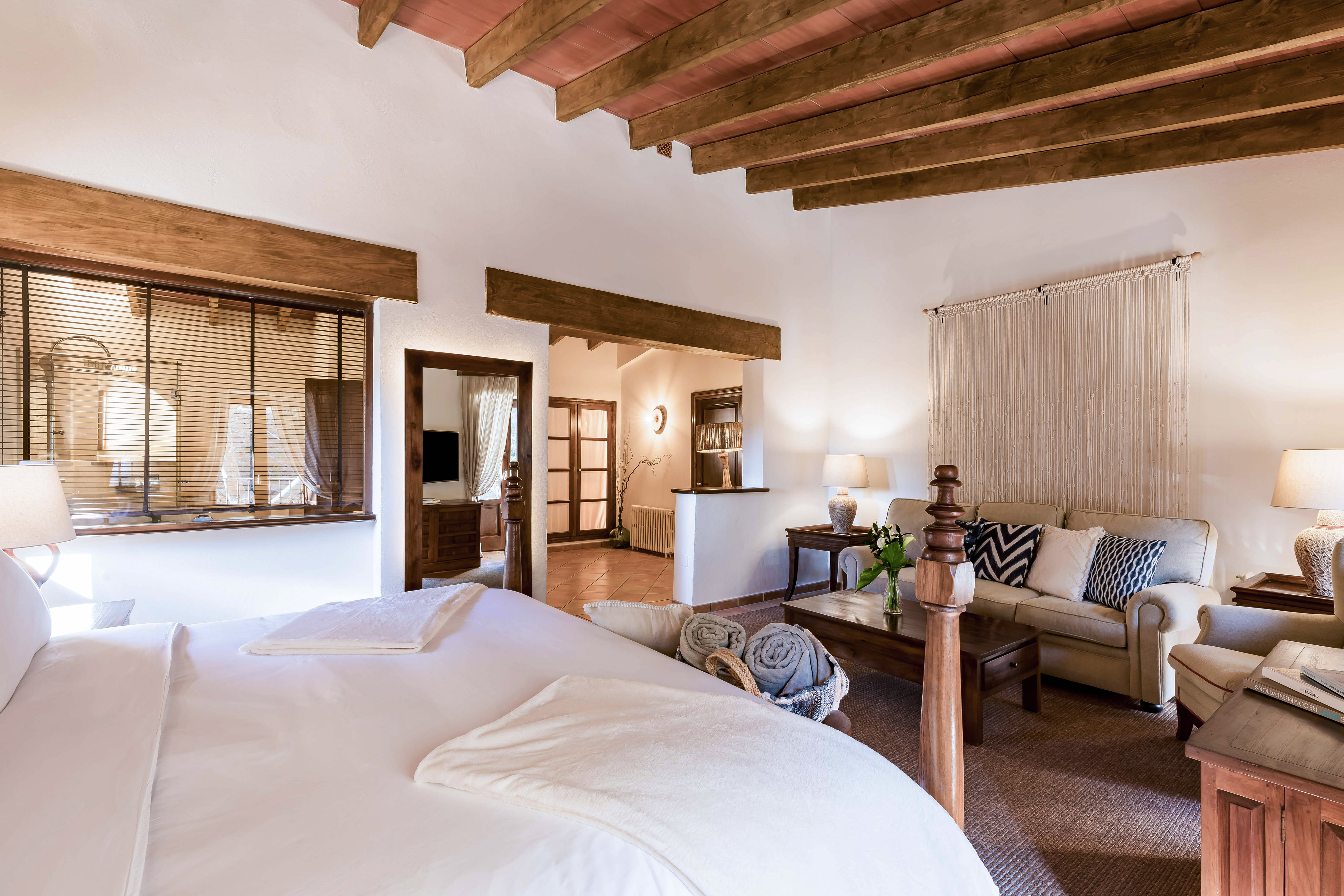 Rustic hotel suite bedroom and living area with wooden beams, warm lighting.