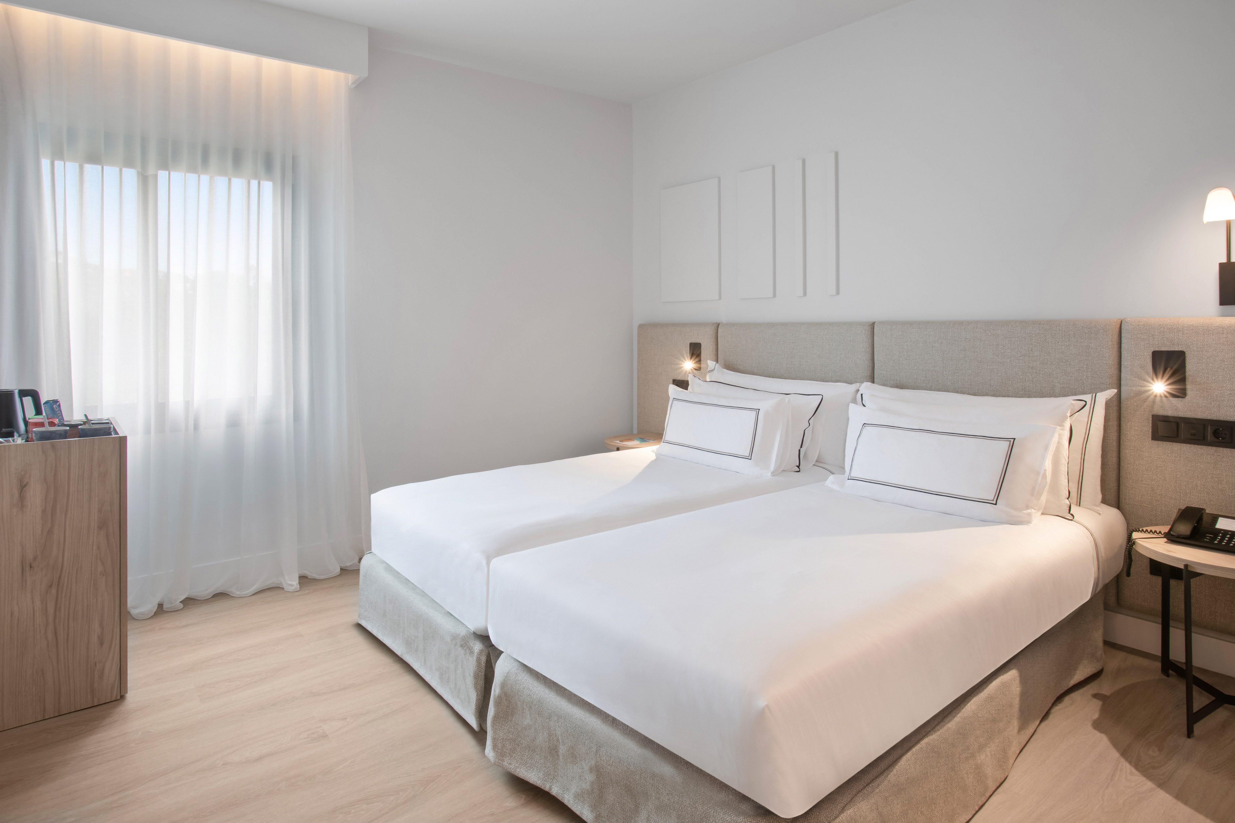 Bright modern hotel room with twin beds, white bedding, and light wood floor.
