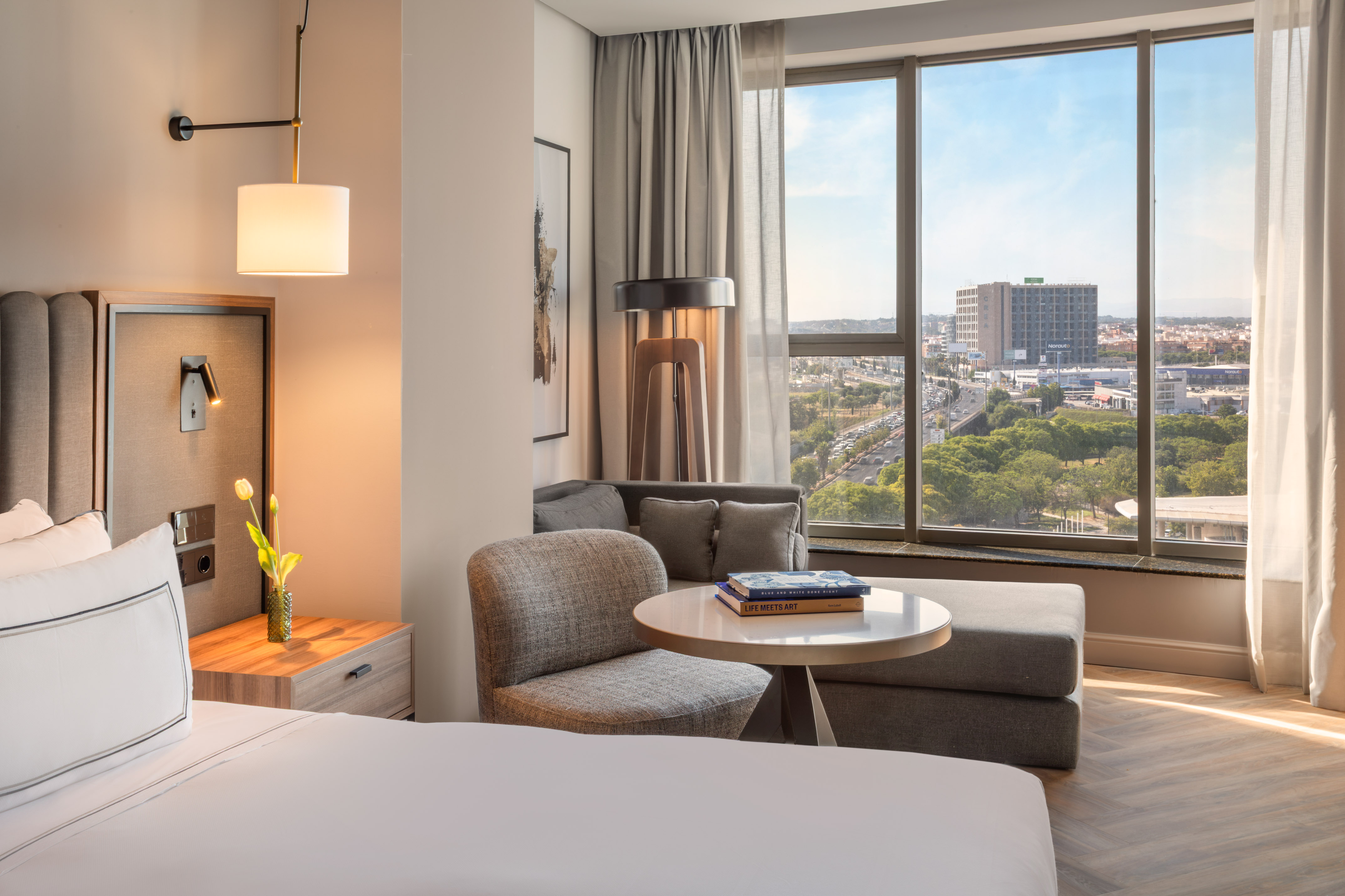 Habitación de hotel moderna con cama, sofá y vistas panorámicas a la ciudad.