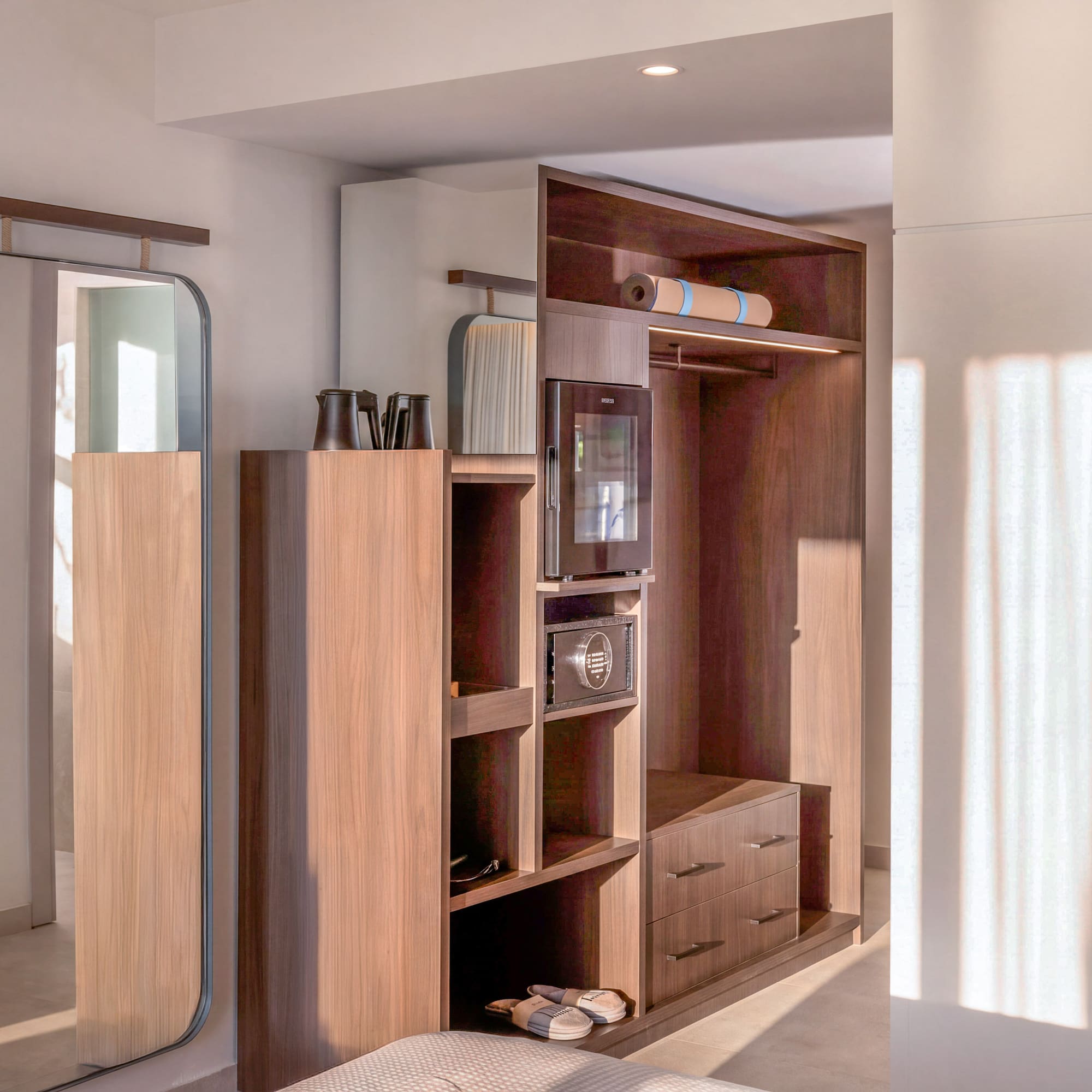 Modern hotel room interior with wooden wardrobe, full-length mirror, minibar, and yoga mat.