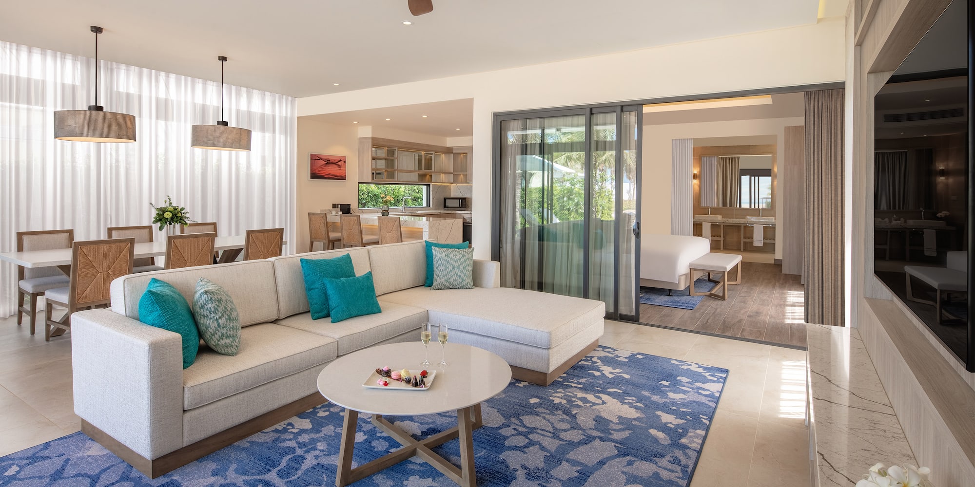 Luxury open-concept suite living room with sectional, blue rug, dining area.