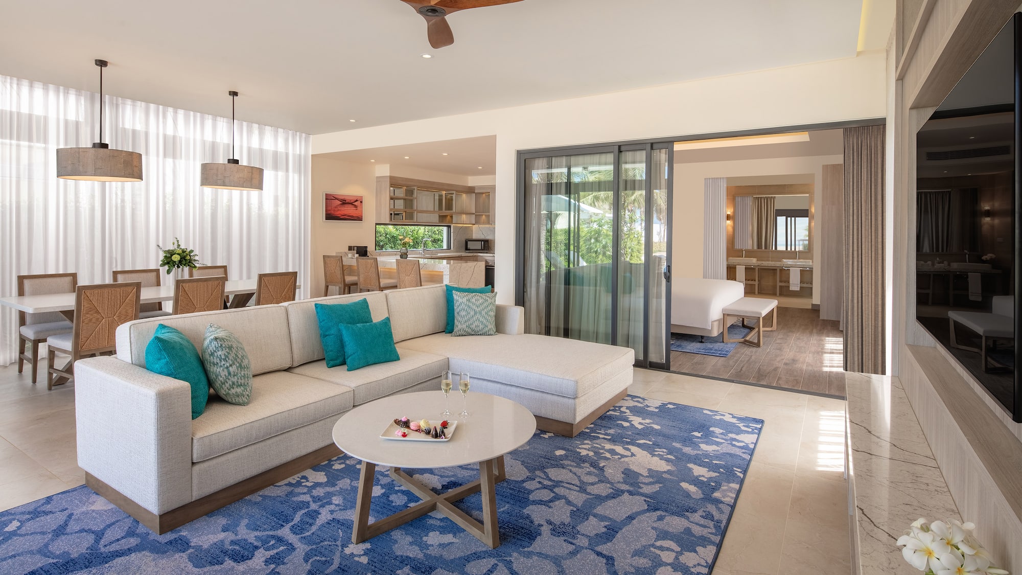 Luxury open-concept suite living room with sectional, blue rug, dining area.