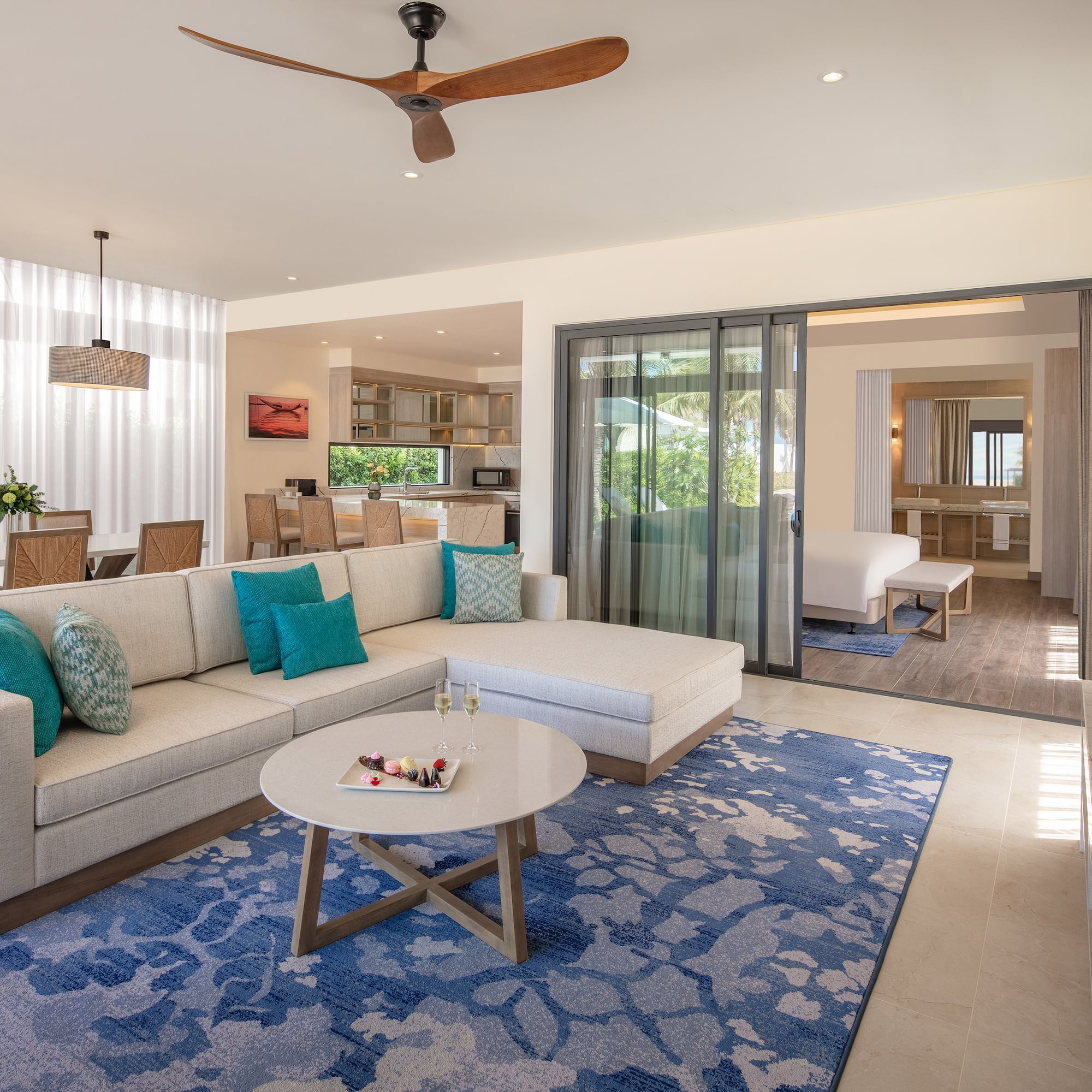 Luxury open-concept suite living room with sectional, blue rug, dining area.