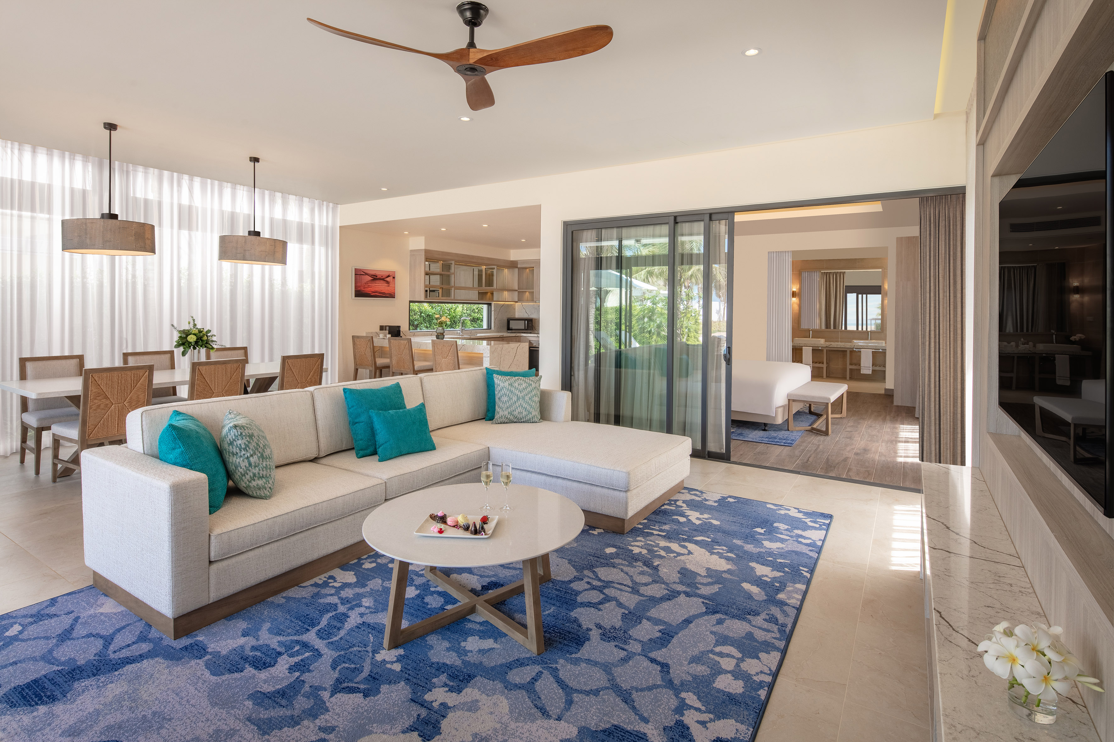 Luxury open-concept suite living room with sectional, blue rug, dining area.