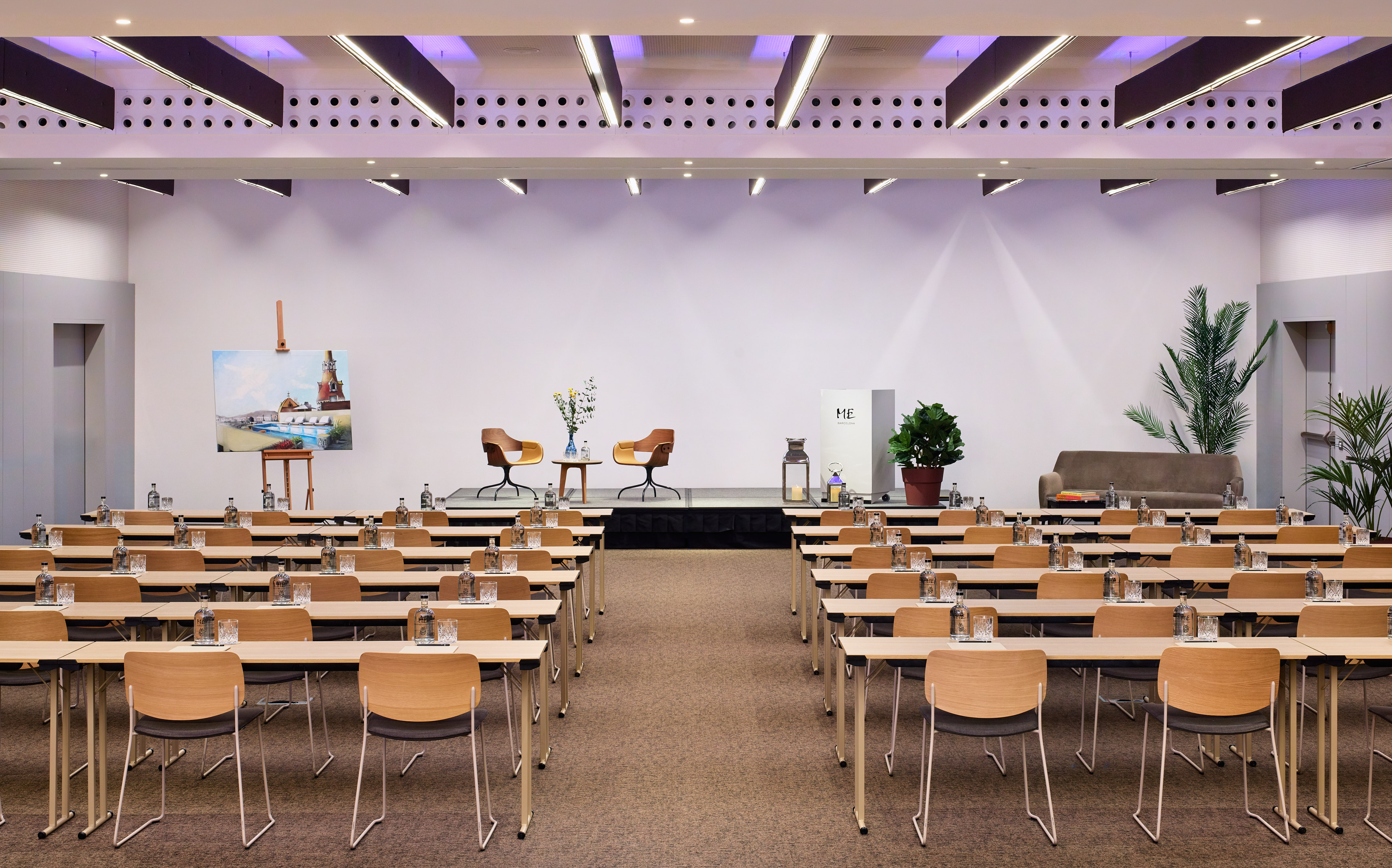 Modern meeting space with rows of tables, chairs, and a presentation stage.