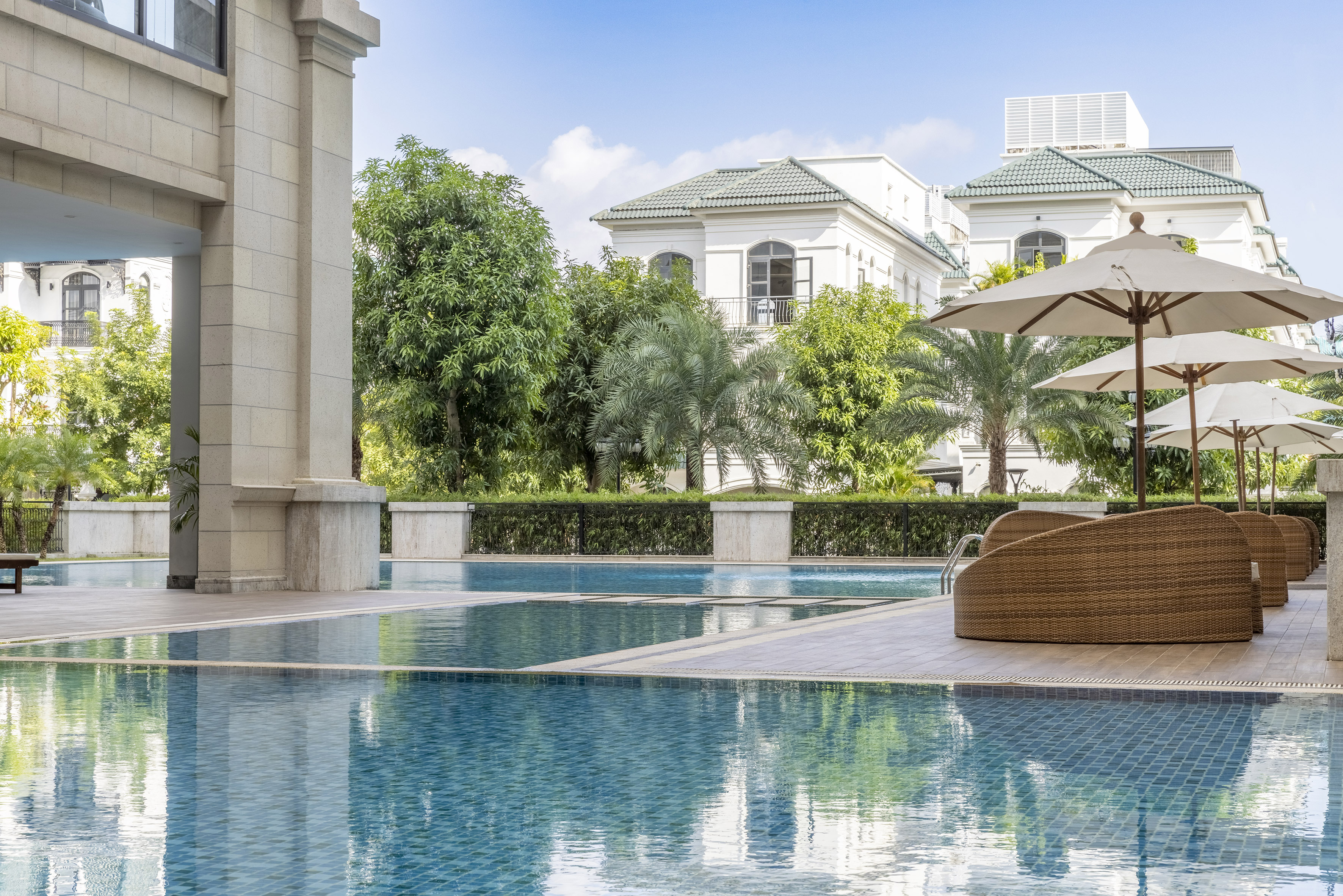 Luxury outdoor pool with modern villas, tropical trees, wicker lounge chairs.