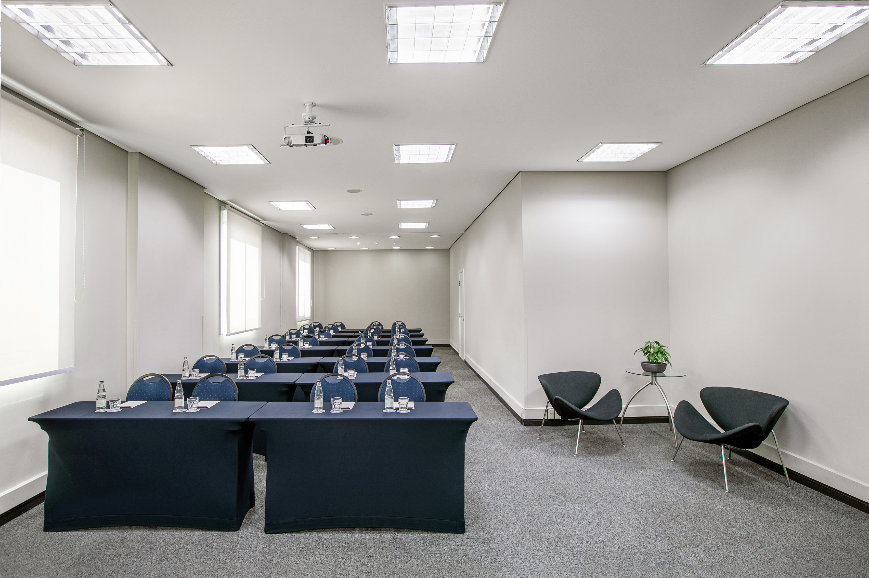 Modern meeting room with blue tables, chairs, projector, and lounge area.
