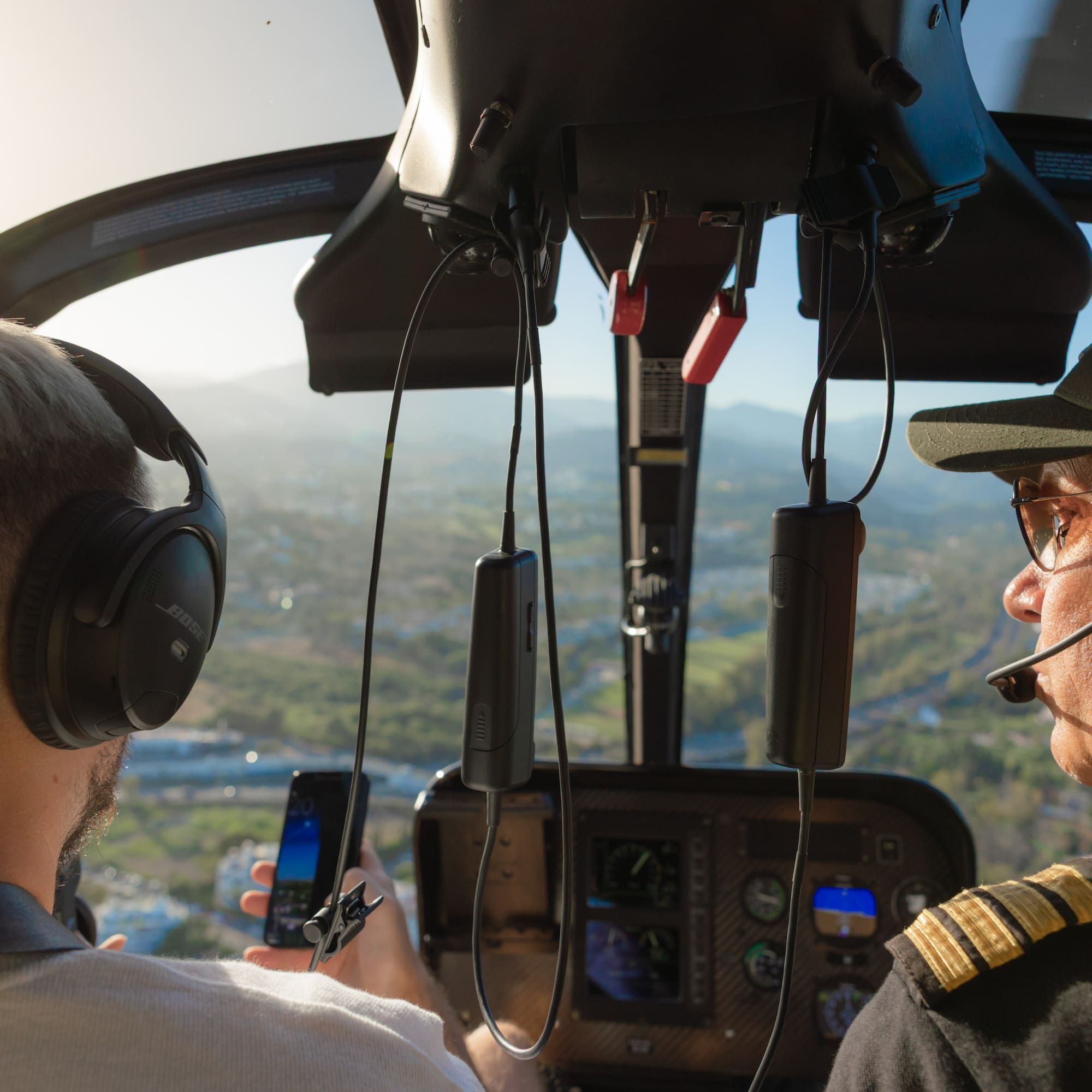 Helicopter pilot and passenger with headphones in cockpit, scenic city flight.