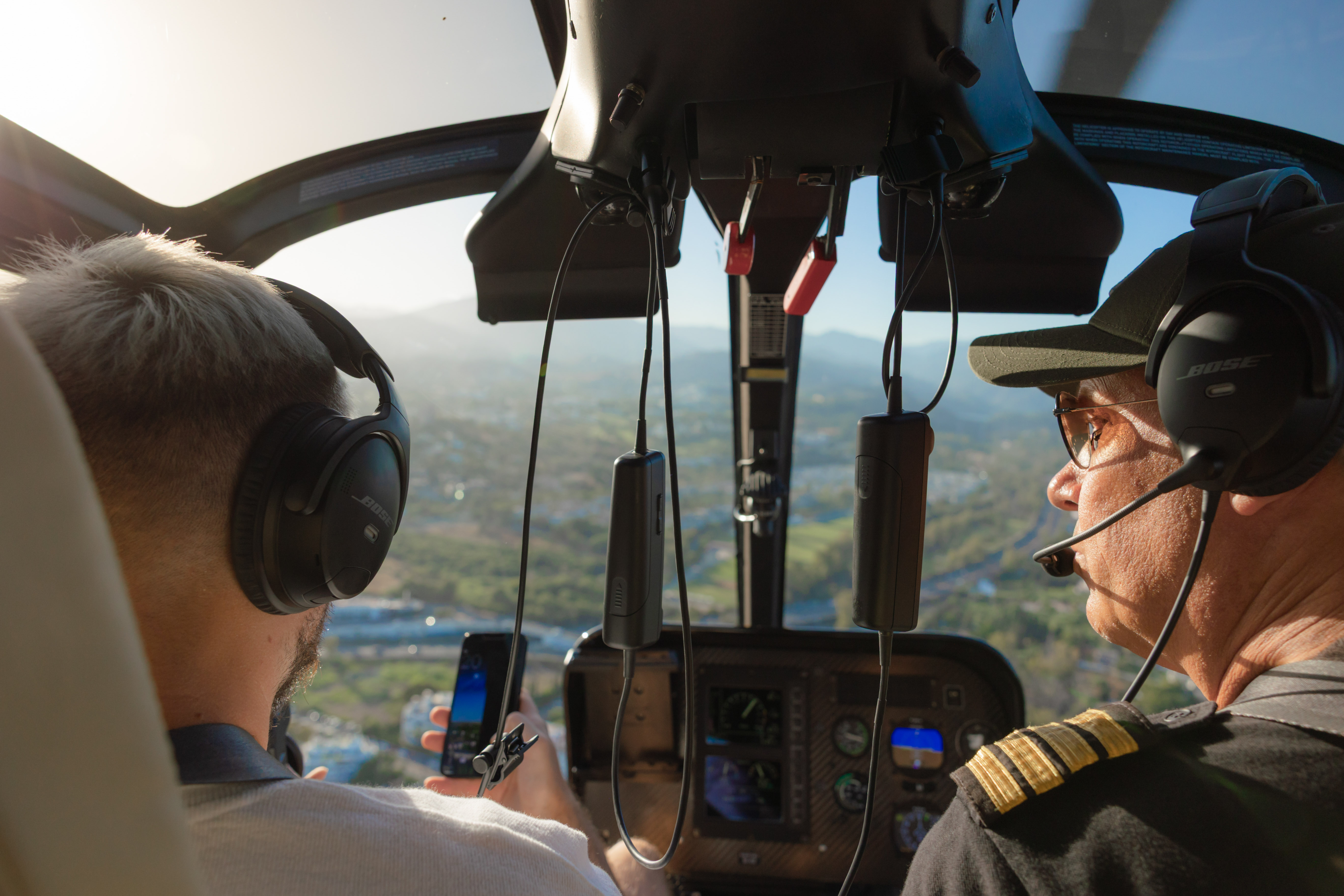 Helicopter pilot and passenger with headphones in cockpit, scenic city flight.