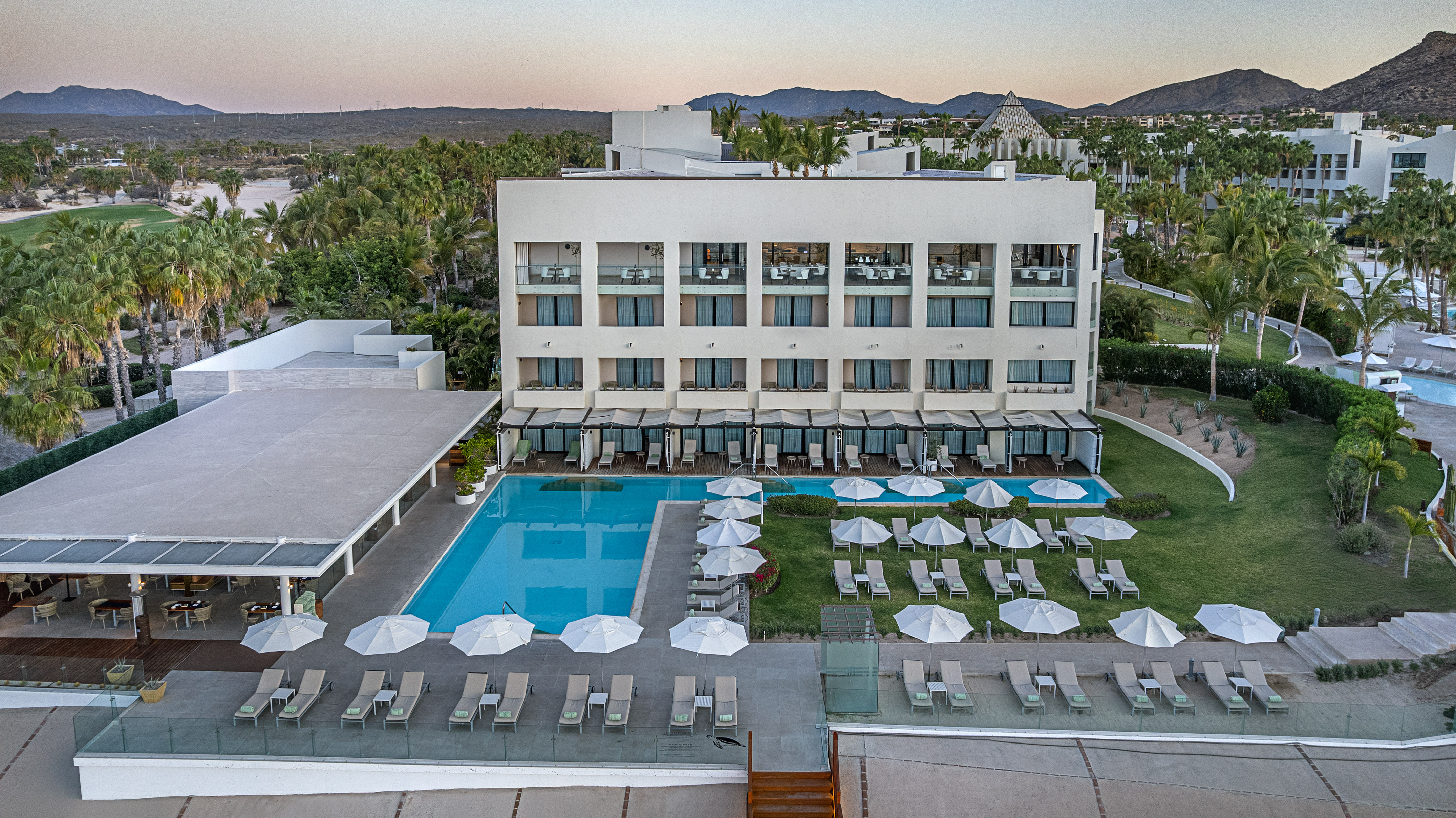 Modern resort hotel with multiple pools, sun loungers, palm trees, and a golf course.