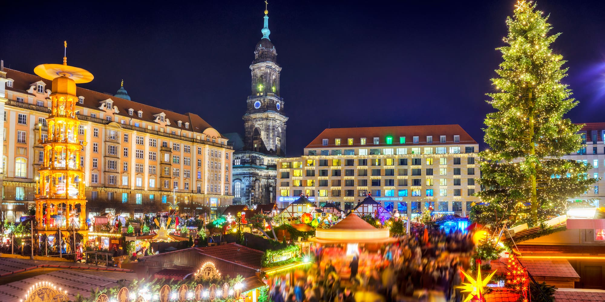 Dresden Striezelmarkt at night with illuminated tree, stalls, carousel, and church.