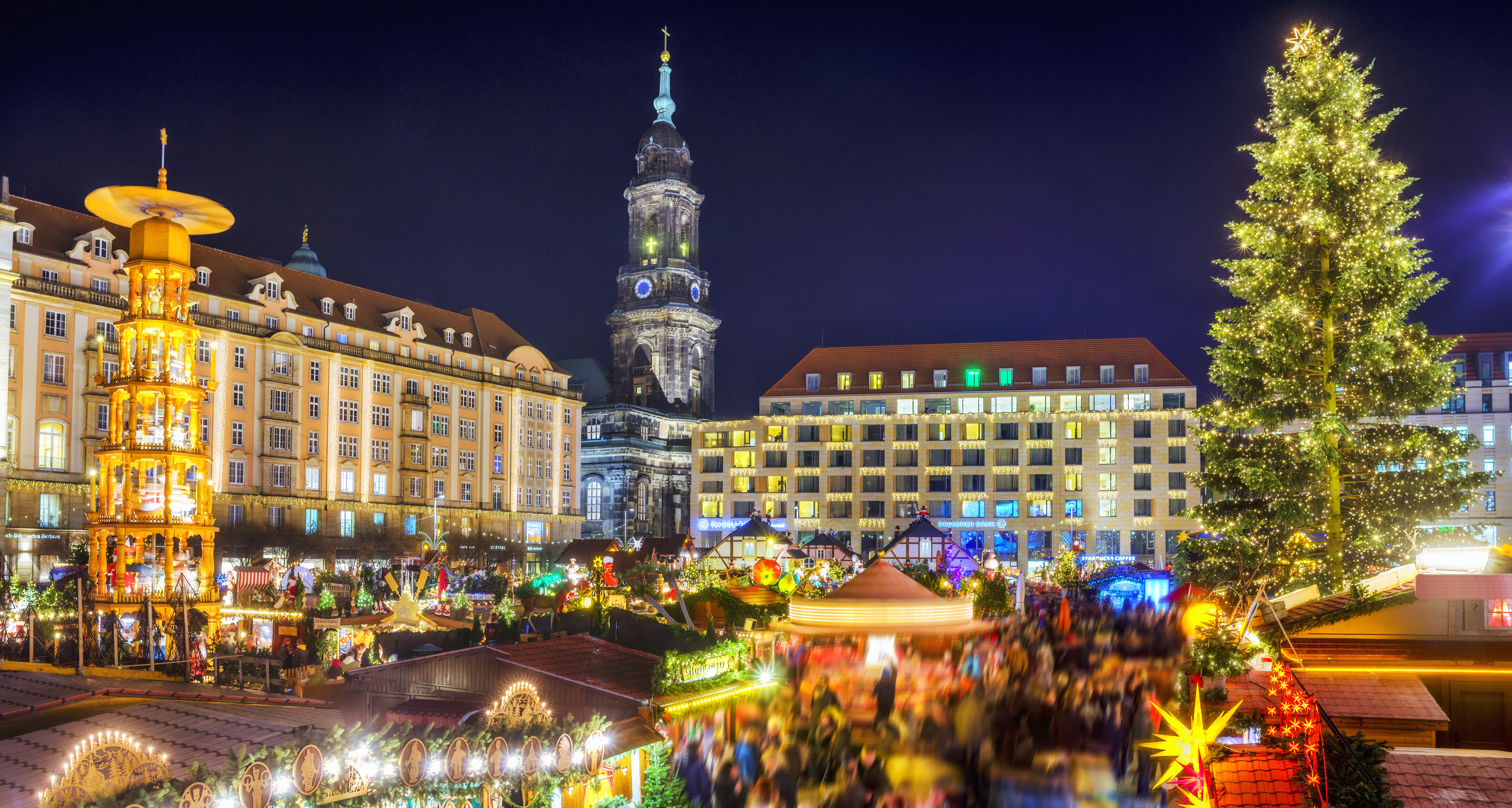 Dresden Striezelmarkt at night with illuminated tree, pyramid, and church tower.