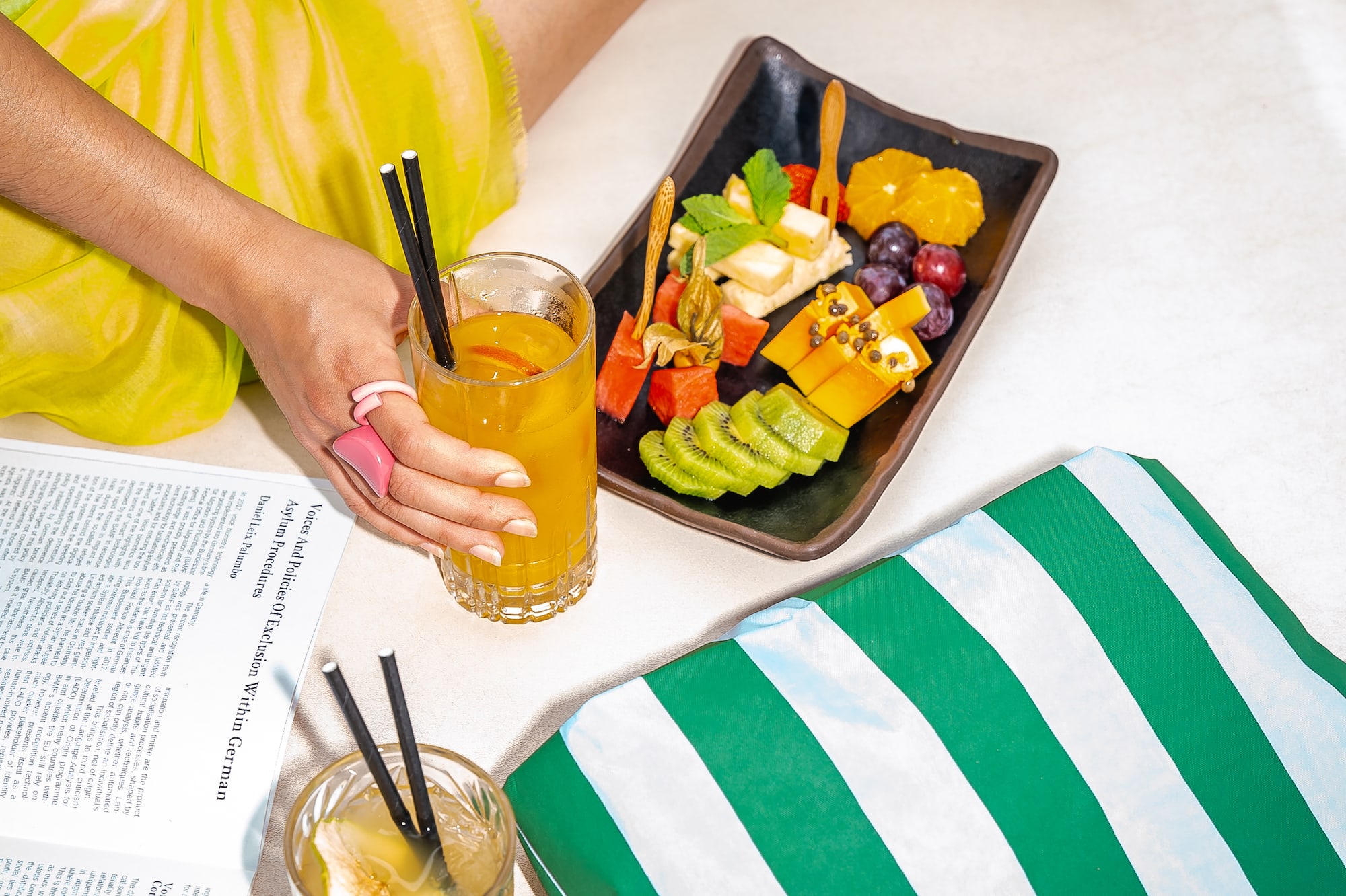 a person holding a glass of juice and a plate of fruit