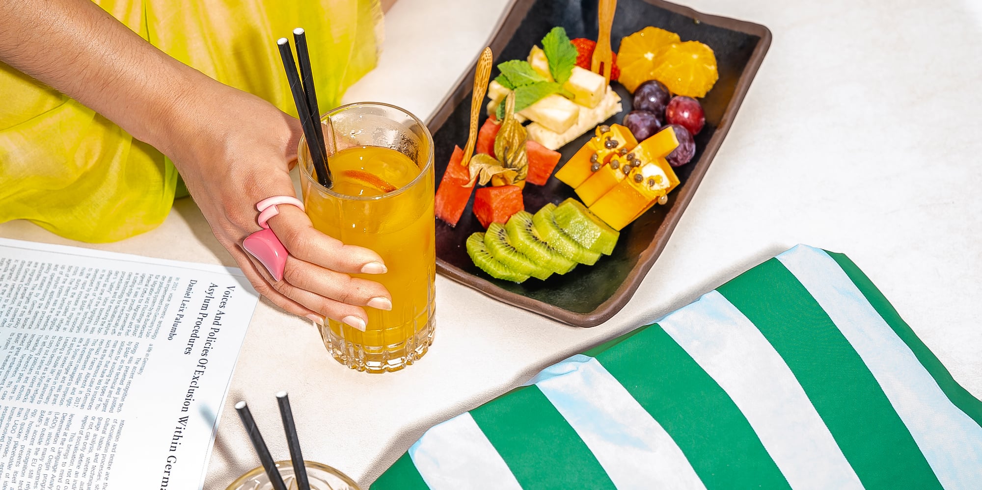 a person holding a glass of juice and a plate of fruit