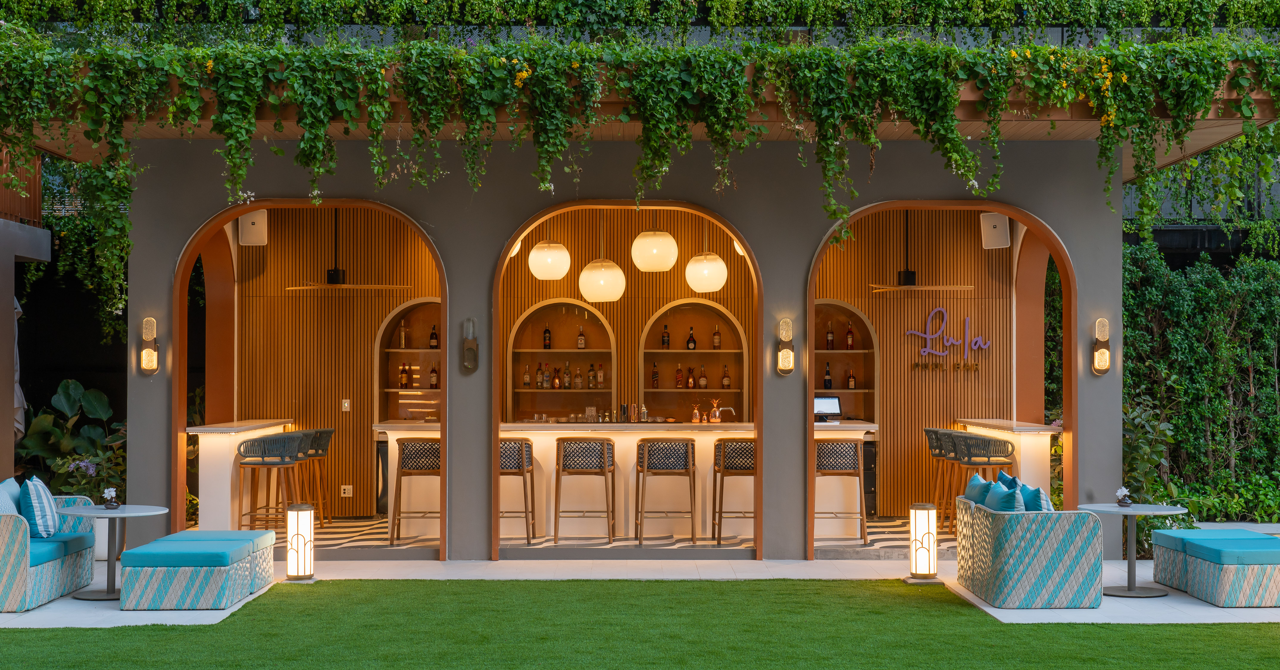 Lush green outdoor pool bar with arched design, bar stools, and lounge seating.