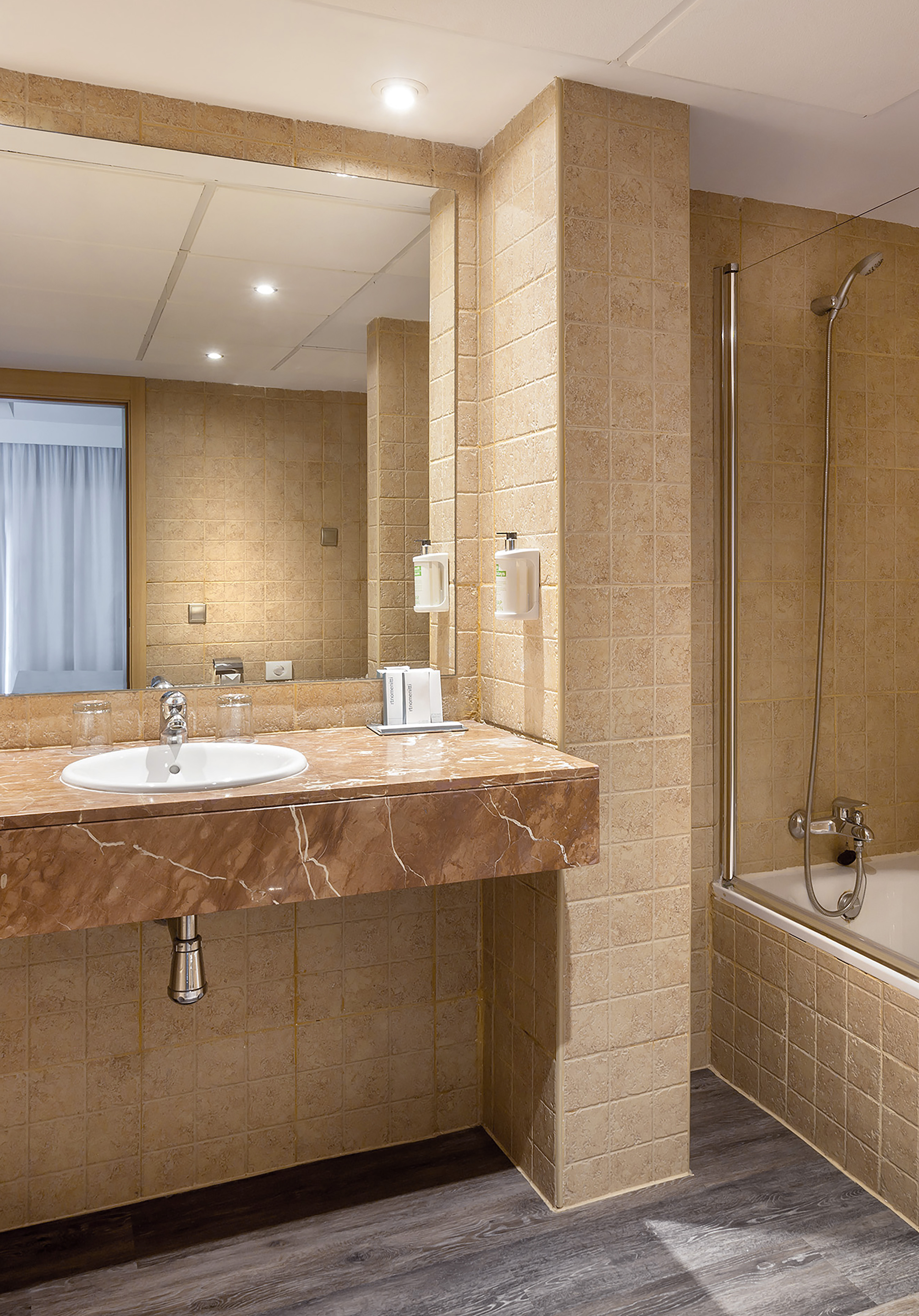Hotel bathroom with marble vanity, white sink, beige tiled walls, and shower bath.