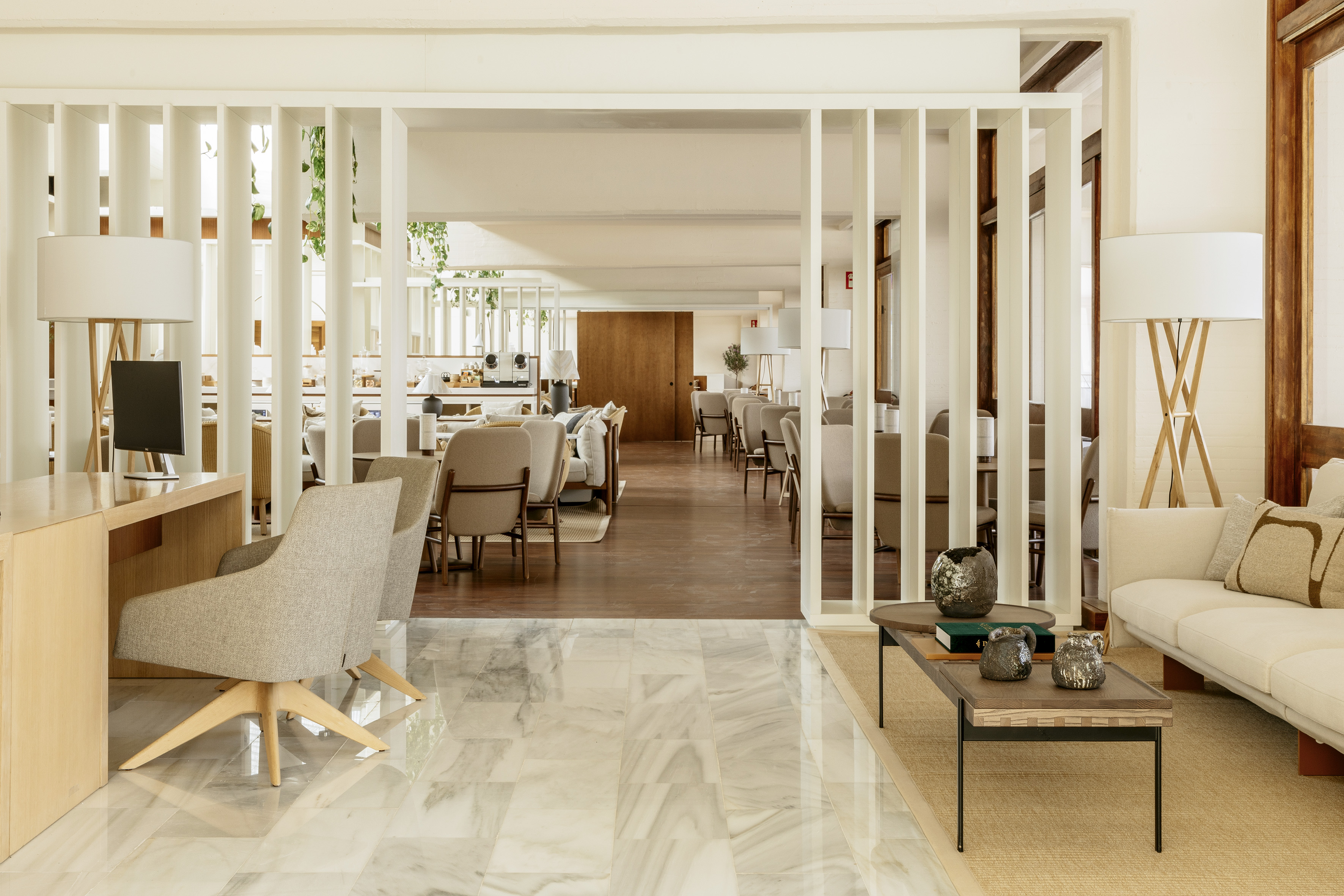 Bright modern hotel lobby with white partitions, light wood furniture, and marble floor.