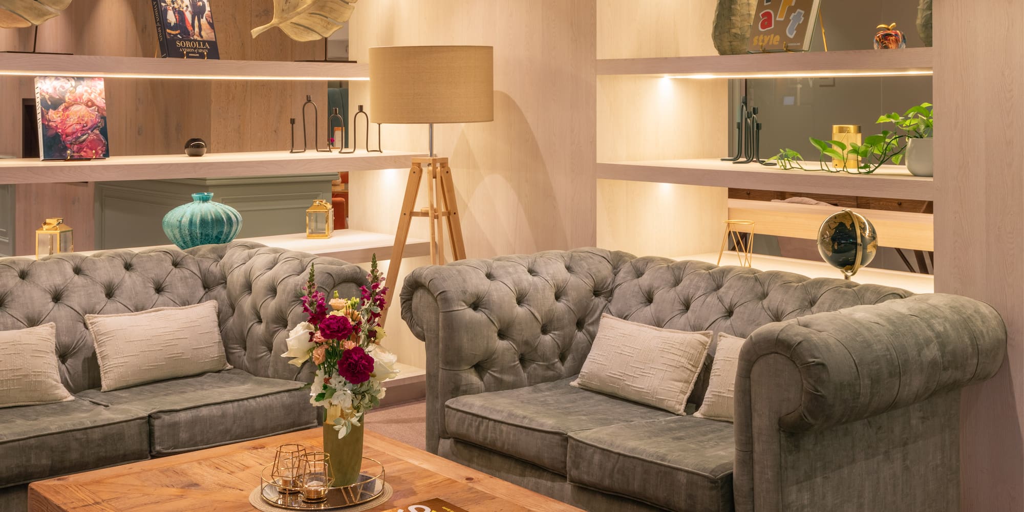 Stylish living room with tufted gray sofas, wood coffee table, and illuminated shelves.