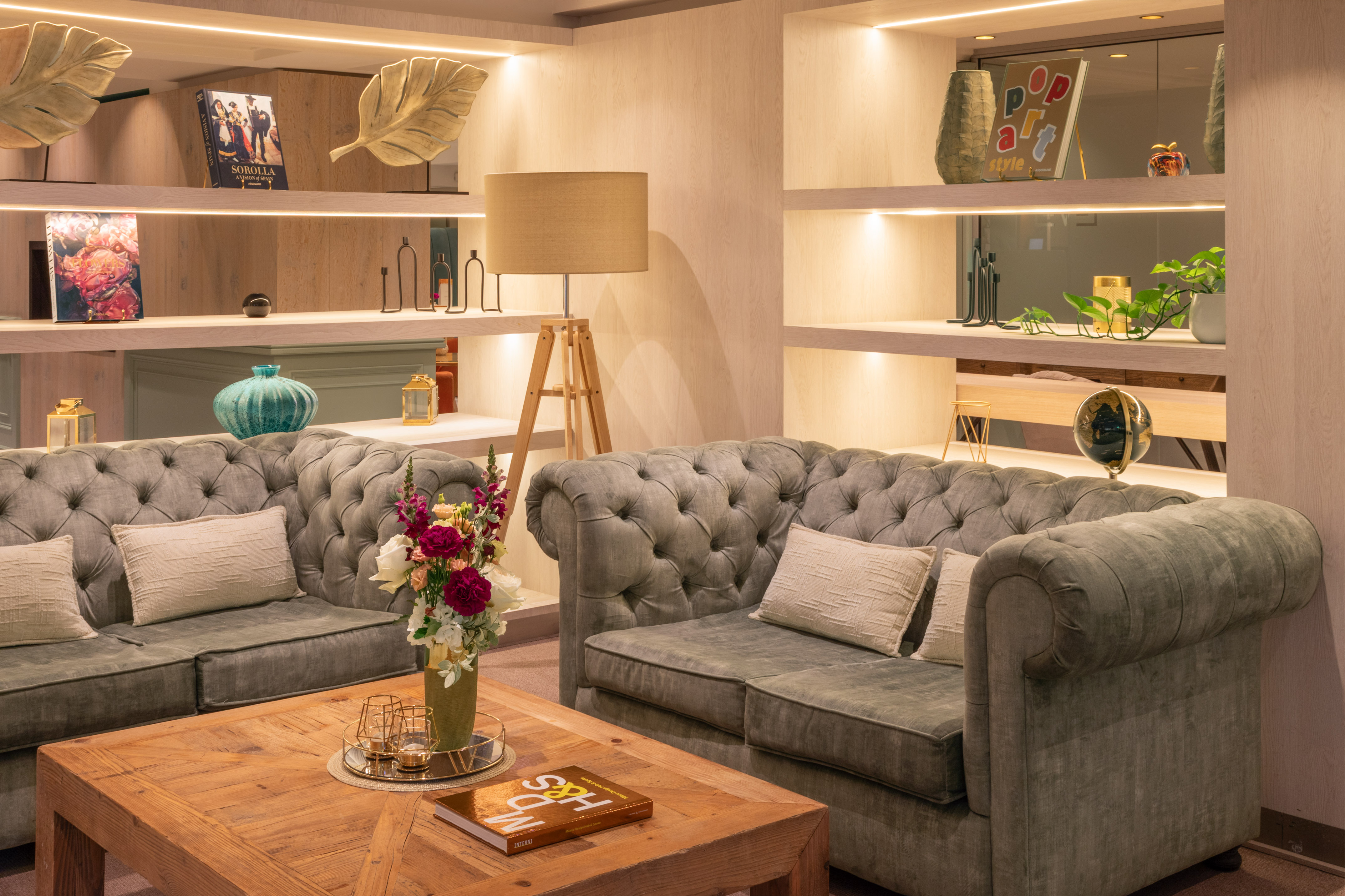 Stylish living room with tufted gray sofas, wood coffee table, and illuminated shelves.