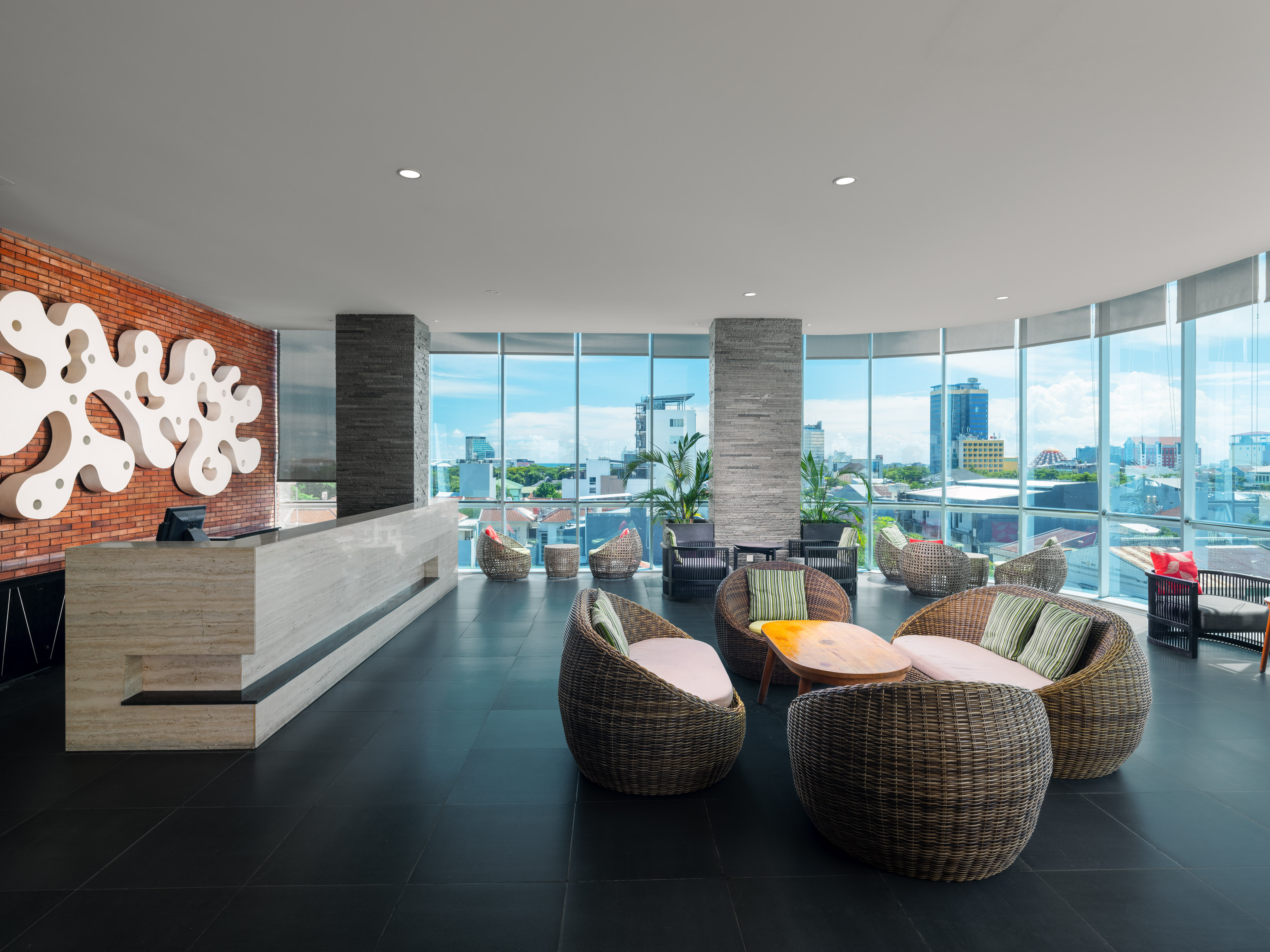 Modern hotel lobby with reception desk, wicker lounge seating, and city view.
