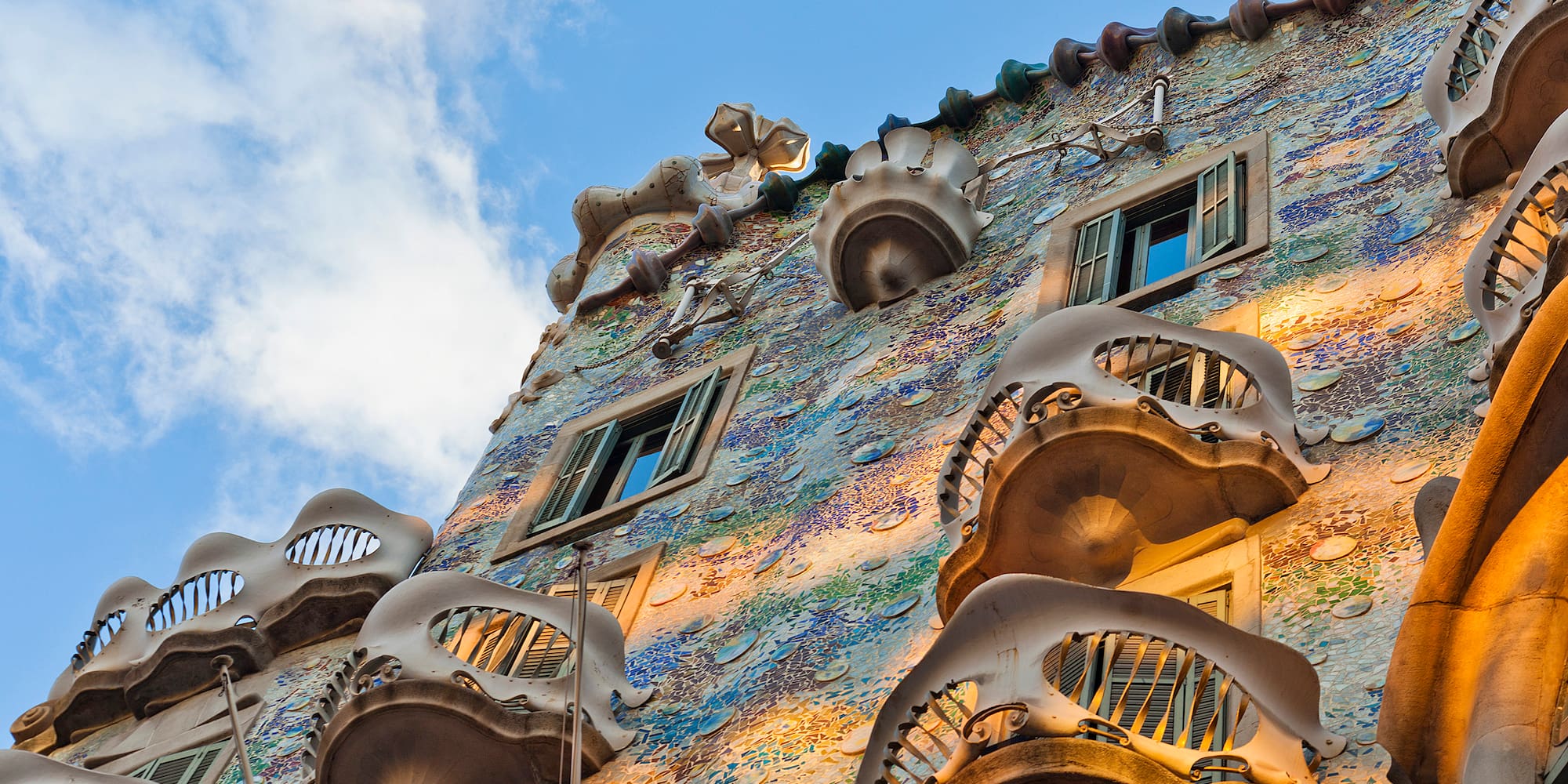 Gaudi's Casa Batlló mosaic facade with skull-like balconies under a blue sky, Barcelona.