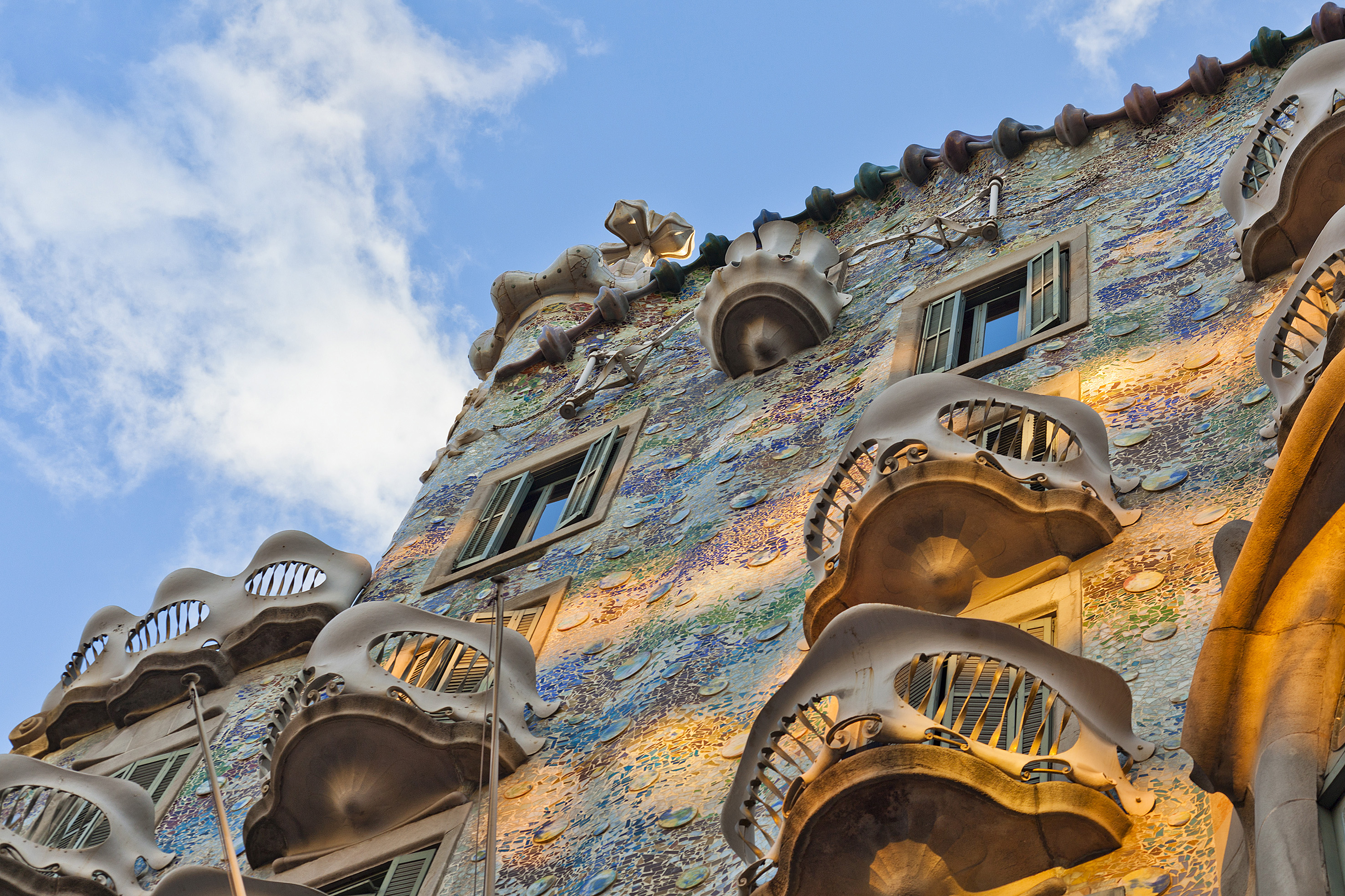 Gaudi's Casa Batlló mosaic facade with skull-like balconies under a blue sky, Barcelona.