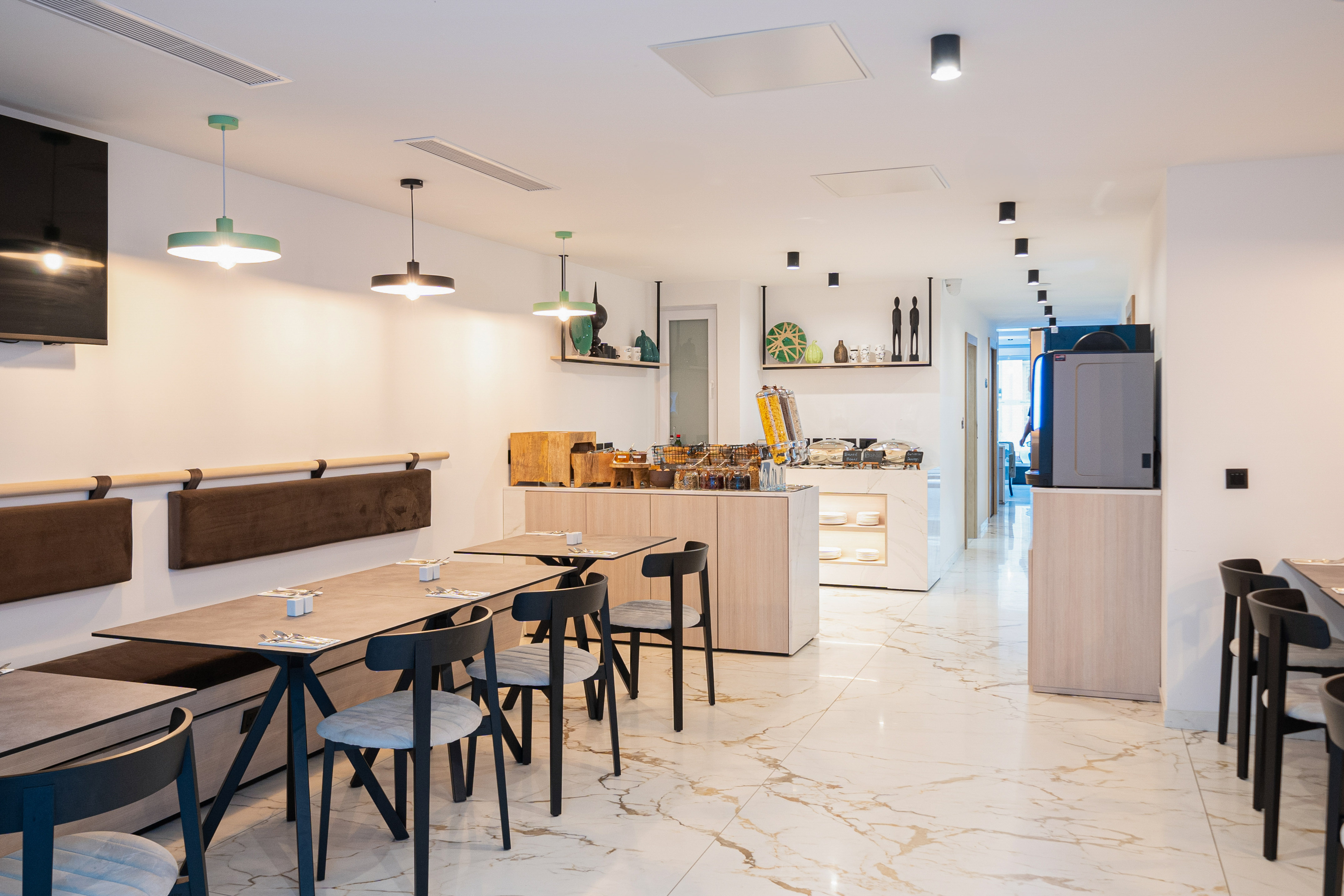 Bright modern hotel breakfast room with buffet station and dining tables.