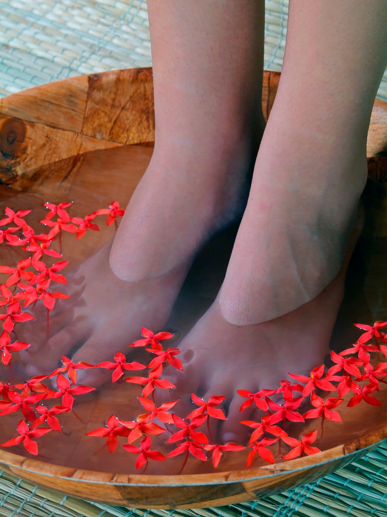 a person's feet in a bowl of water with red flowers