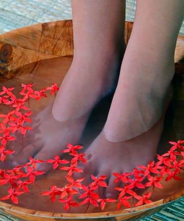 a person's feet in a bowl of water with red flowers