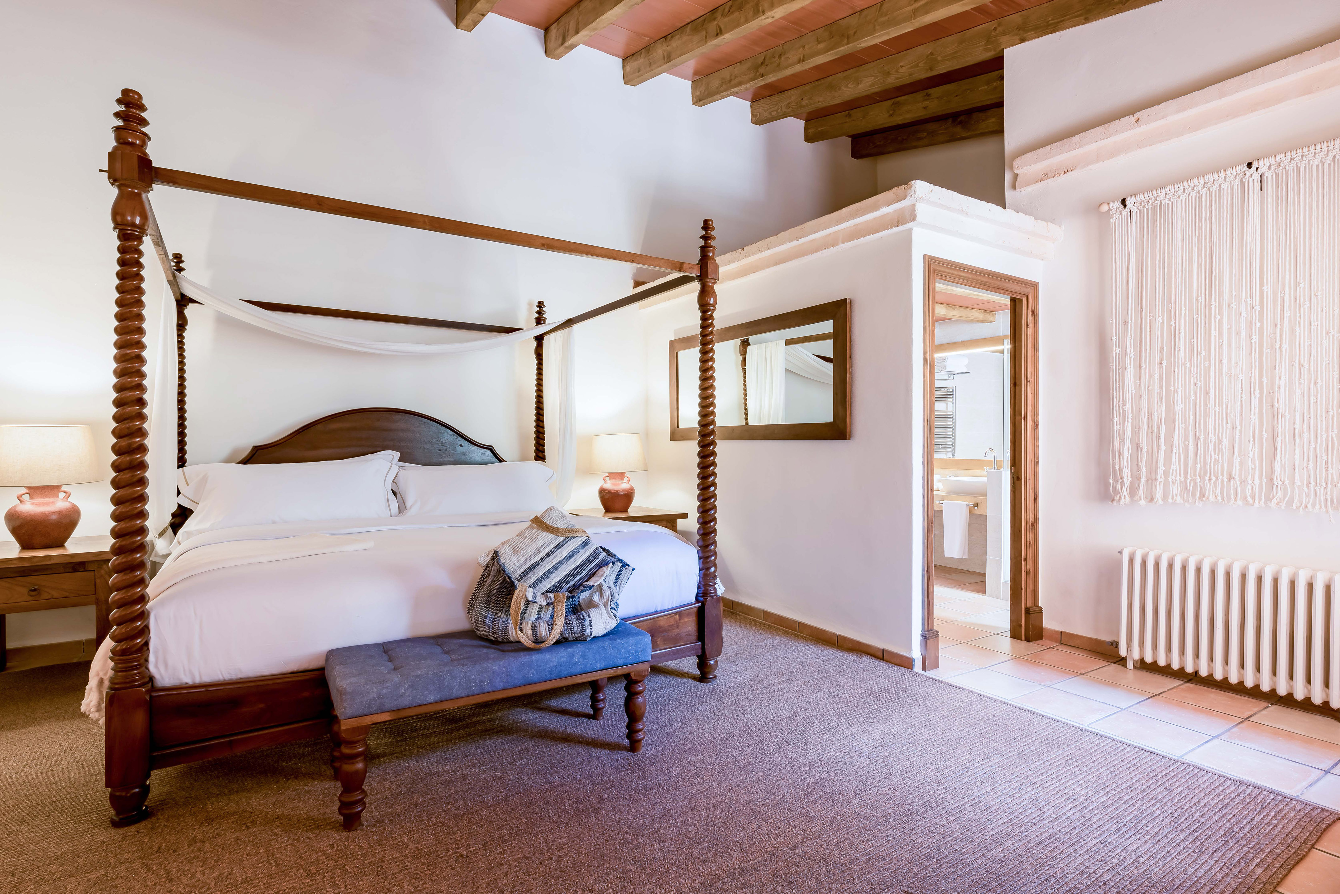 Rustic bedroom with carved four-poster bed, exposed wood beams, and blue bench.