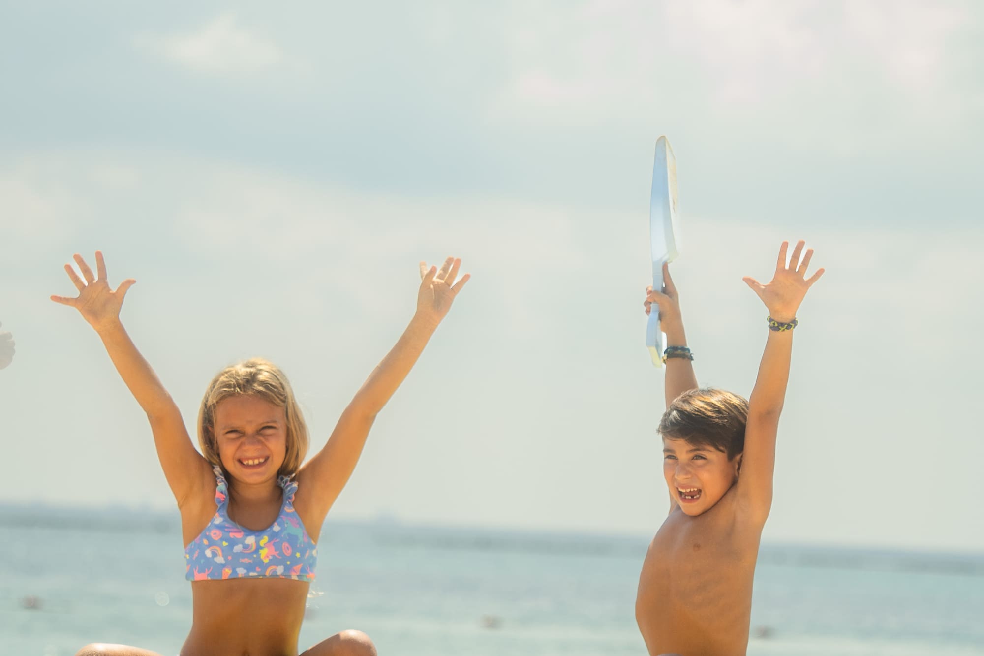 Niños sonrientes jugando en la playa con castillos de arena y mar de fondo.