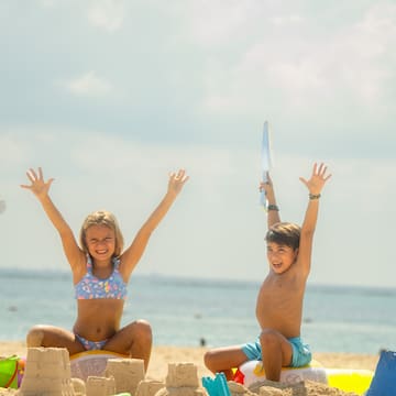 a boy and girl sitting on sand with sandcastles