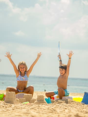 a boy and girl sitting on sand with sandcastles