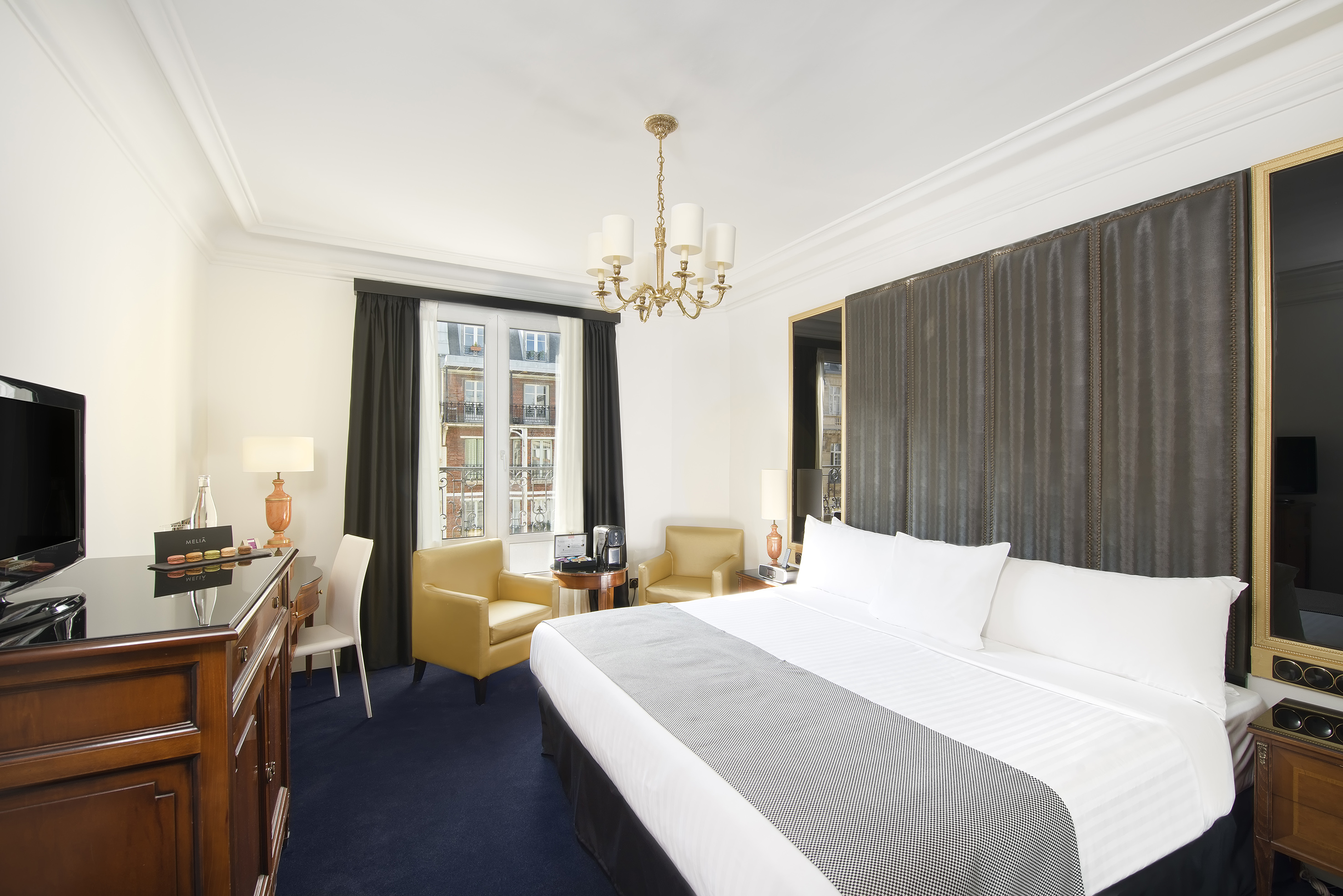 Elegant hotel bedroom with king bed, desk, seating area, and chandelier.