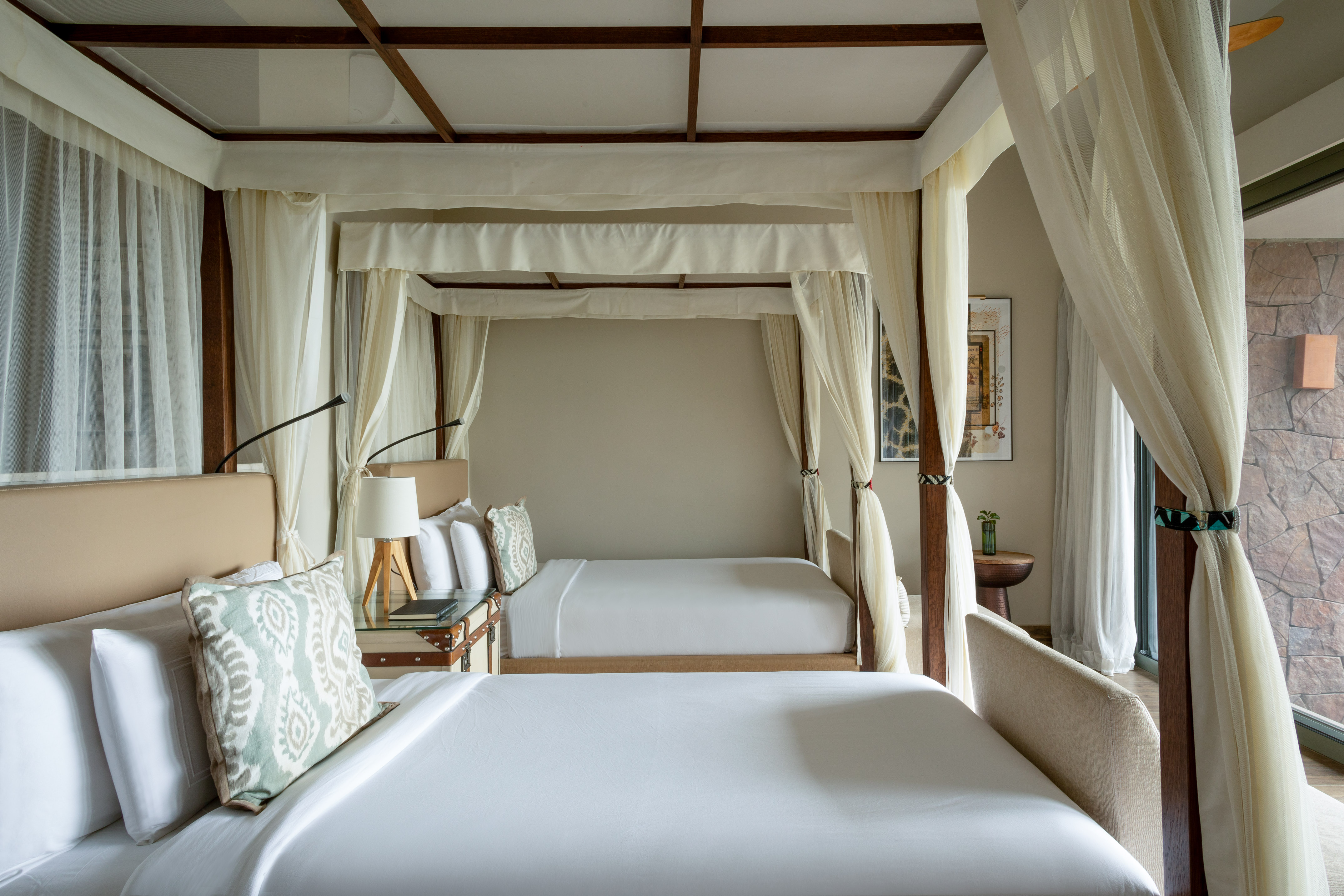 Luxury hotel room with two elegant canopy beds, white drapes, and wooden frames.