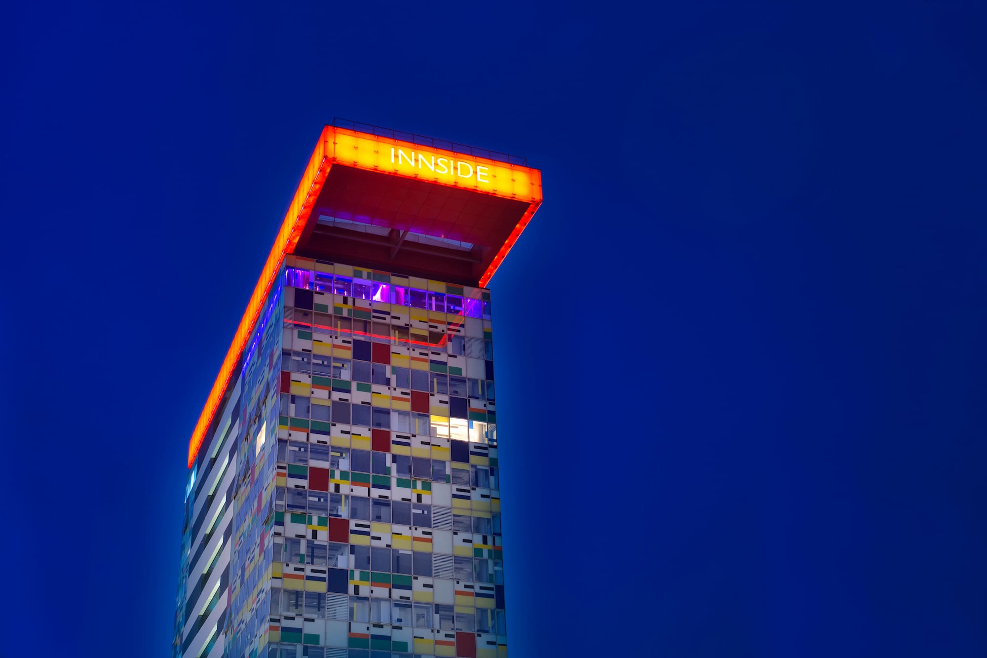 INNSIDE hotel, modern skyscraper with colorful illuminated facade at night.