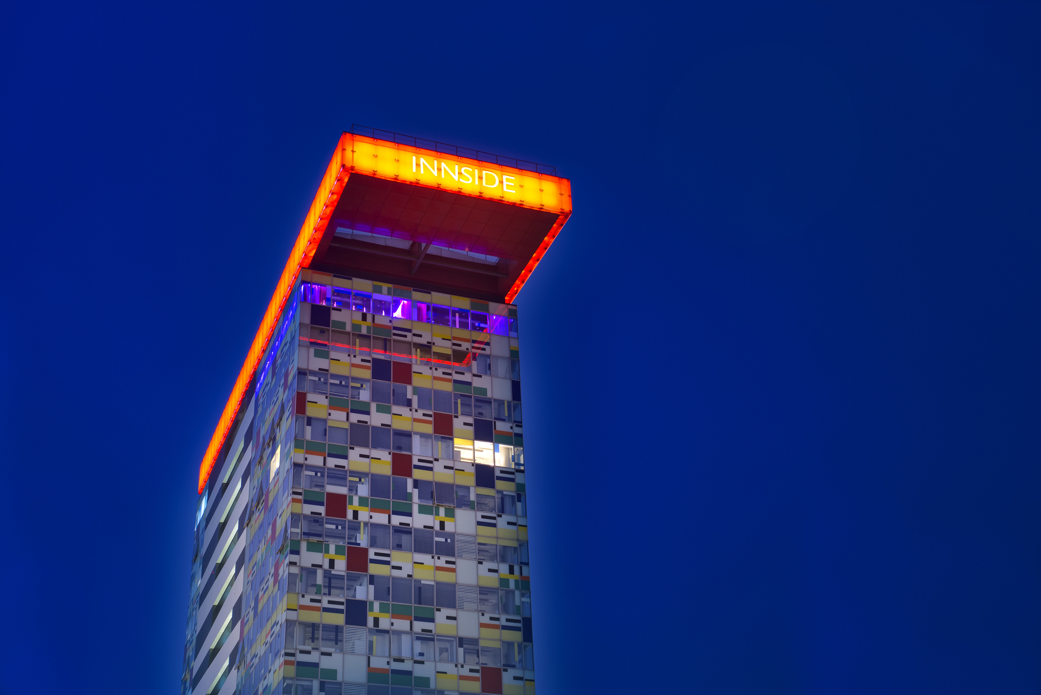 INNSIDE hotel, modern skyscraper with colorful illuminated facade at night.